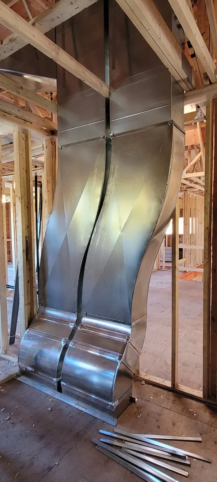 Metal ductwork being installed within the wooden framing of a building under construction.