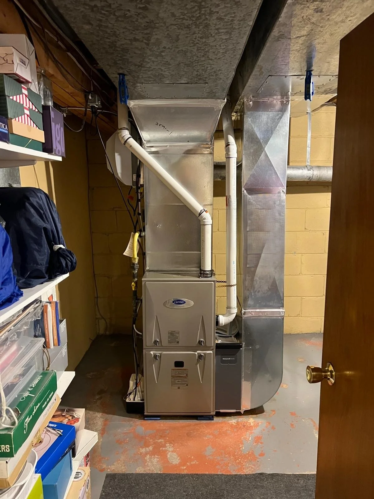 Furnace and duct system in a basement utility room, with shelves and storage on the side.