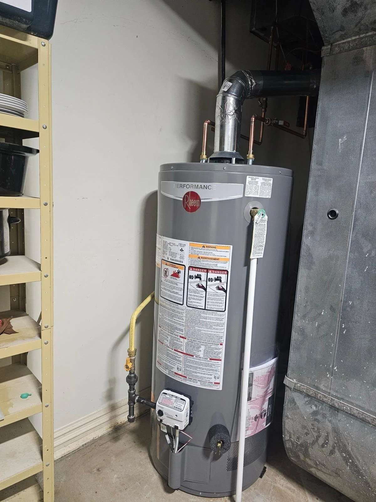 A Rheem water heater in a utility room, with various warning labels and a vent pipe on top.