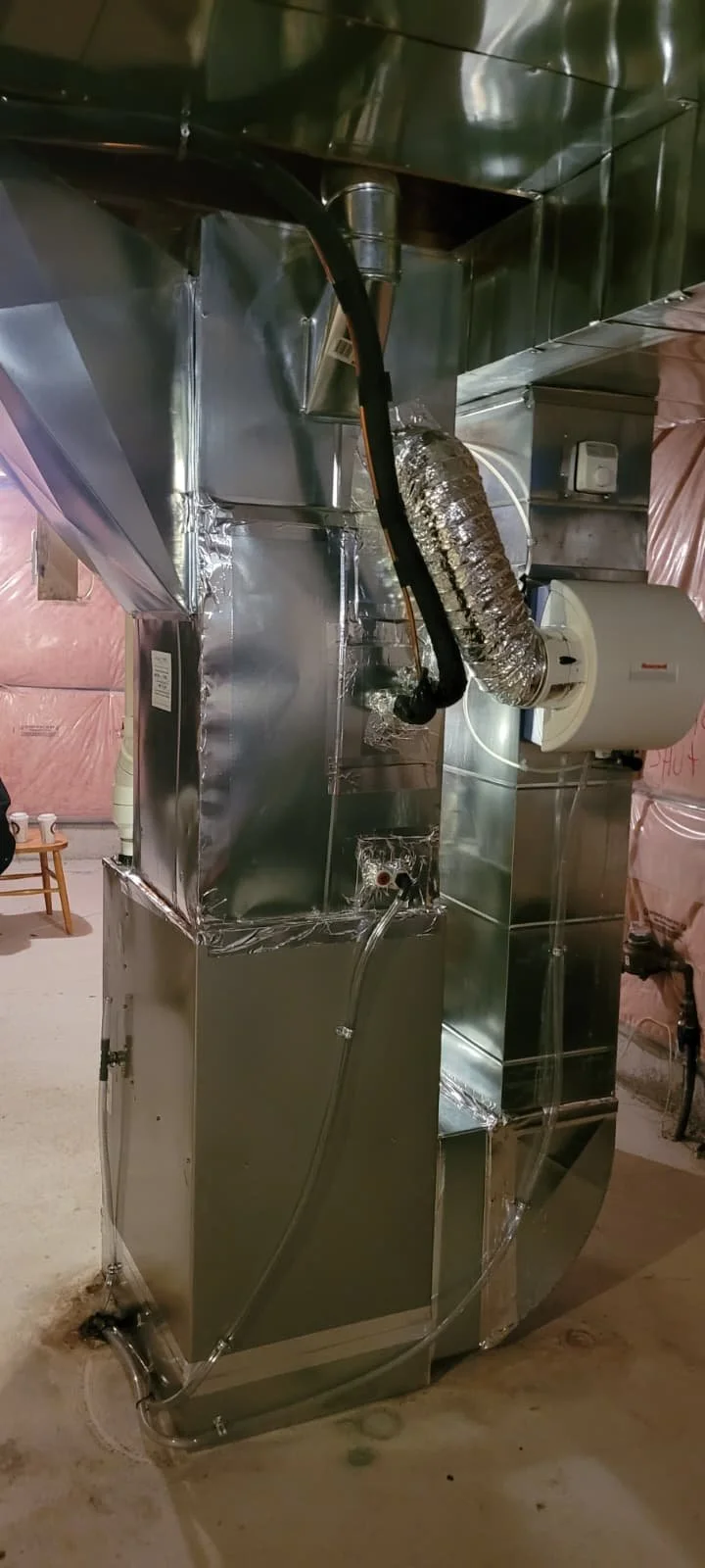 Metal HVAC ventilation system with insulated flexible duct and a round appliance in an unfinished basement.