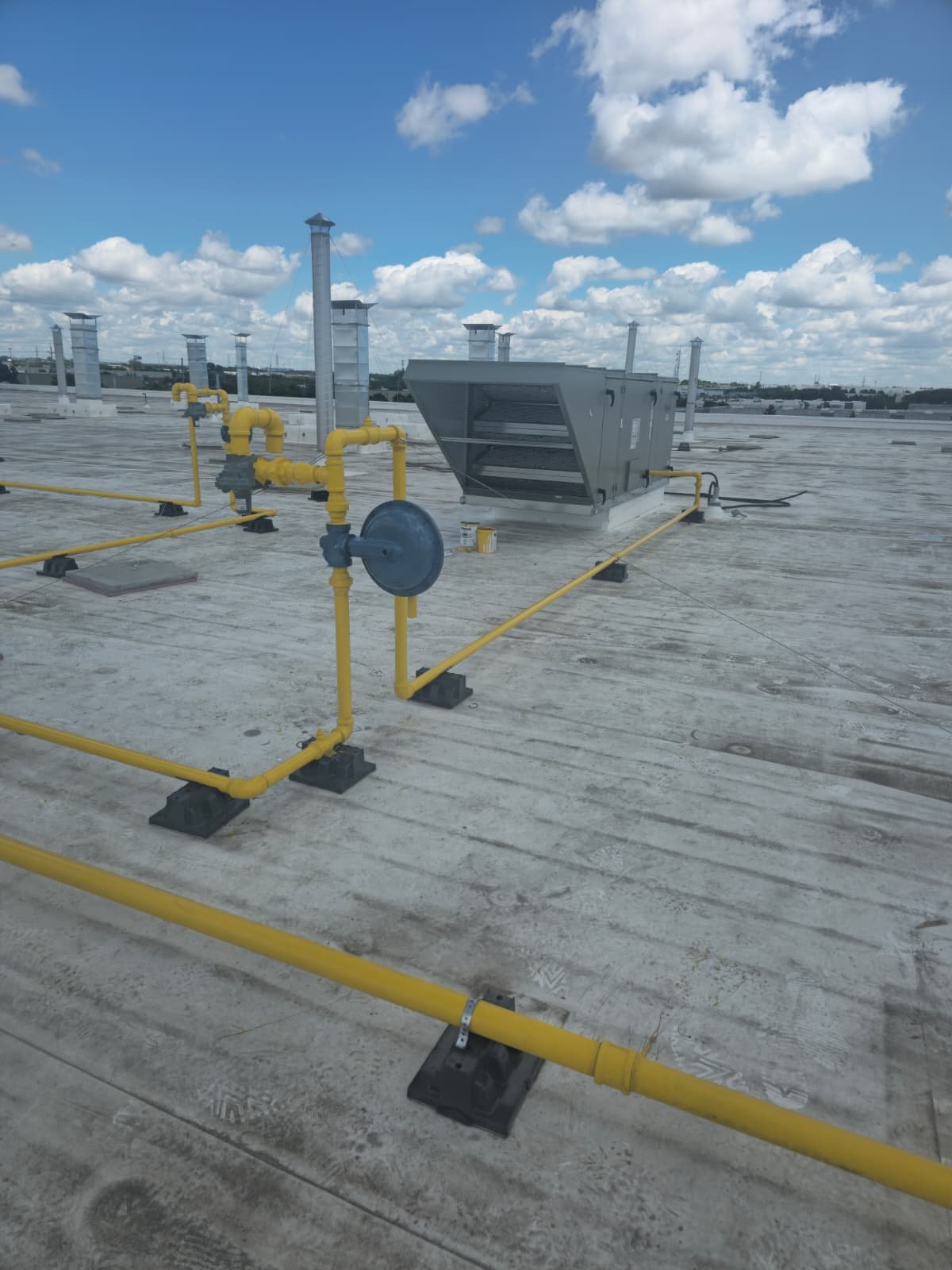 Rooftop with yellow gas pipes and mechanical equipment under a partly cloudy sky.