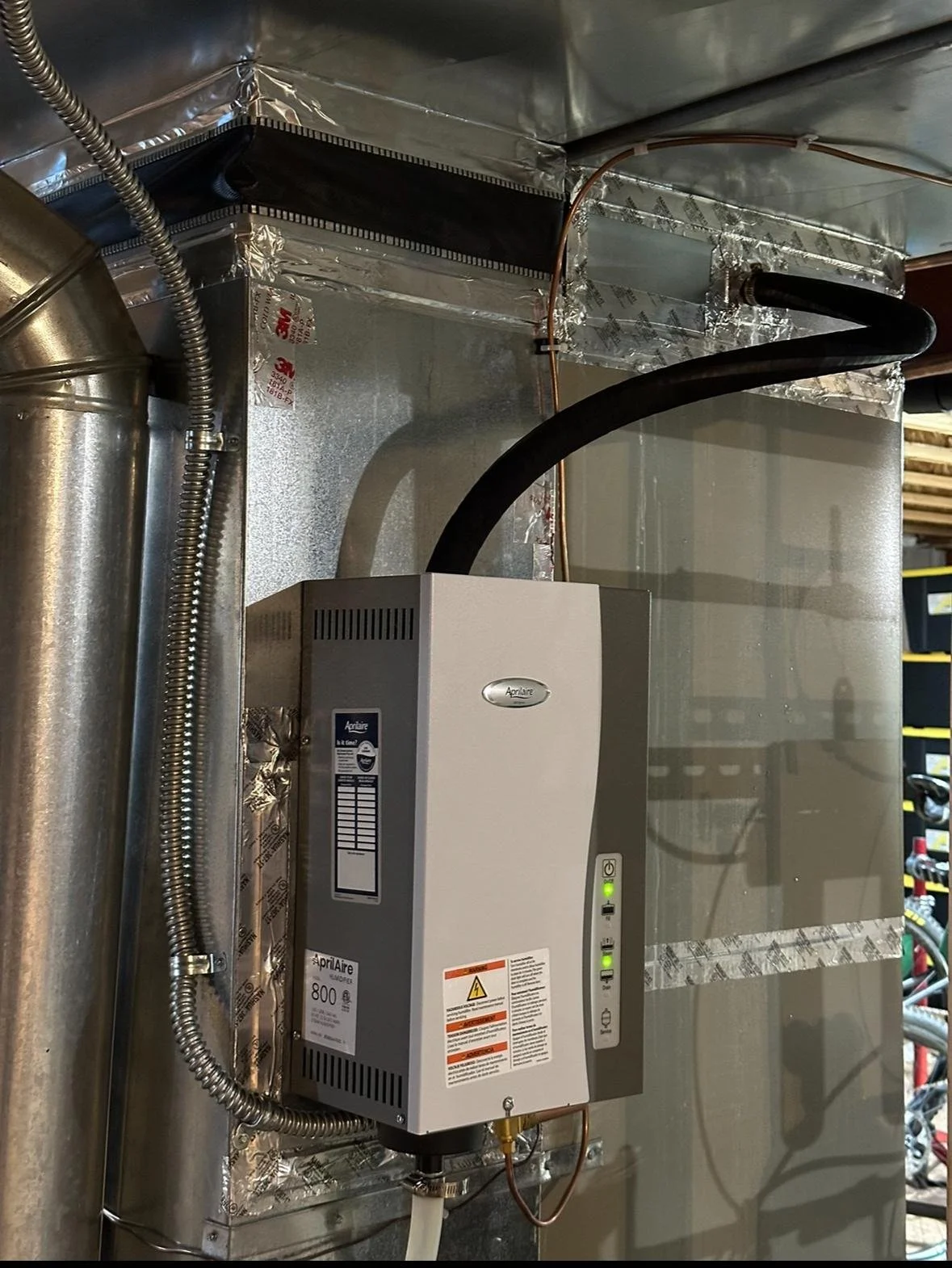 This is an HVAC or ventilation system with an APRilaire filter and electronic control unit mounted on a metallic wall with insulated ducts and cables.