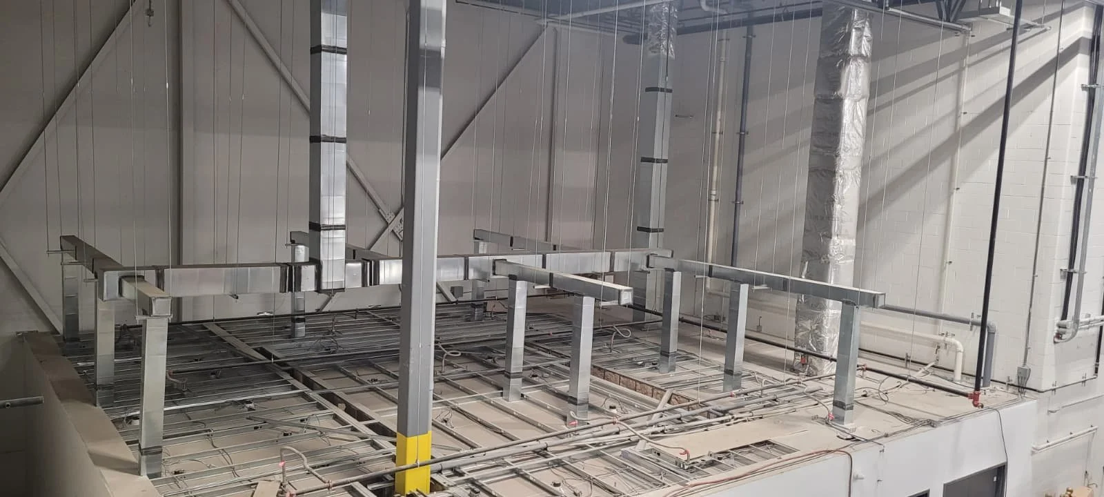 Structural framework of an industrial or mechanical room with metal beams, pipes, and electrical wiring.