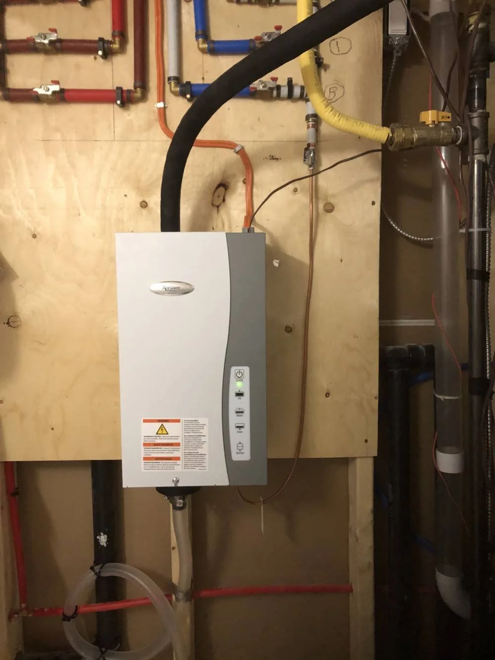 A water heater mounted on a wooden wall with various pipes and fittings connected to it.