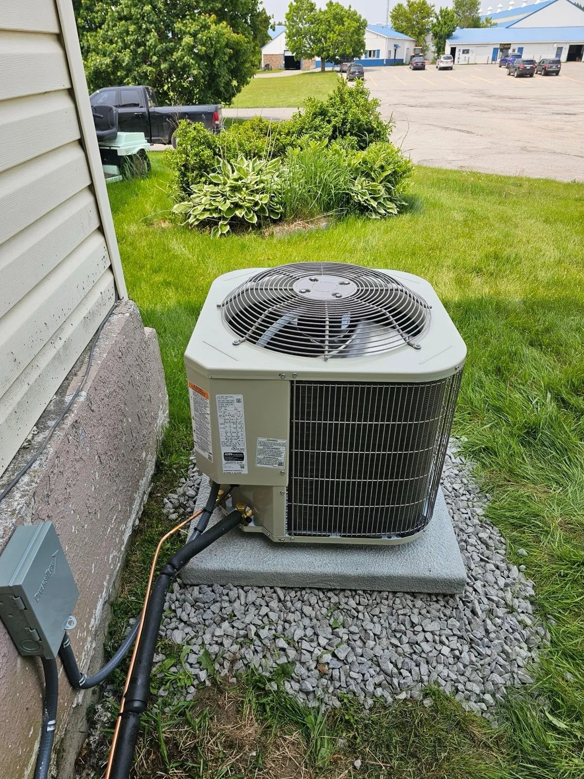 An outdoor air conditioning unit installed next to a house, sitting on a concrete pad surrounded by grass.