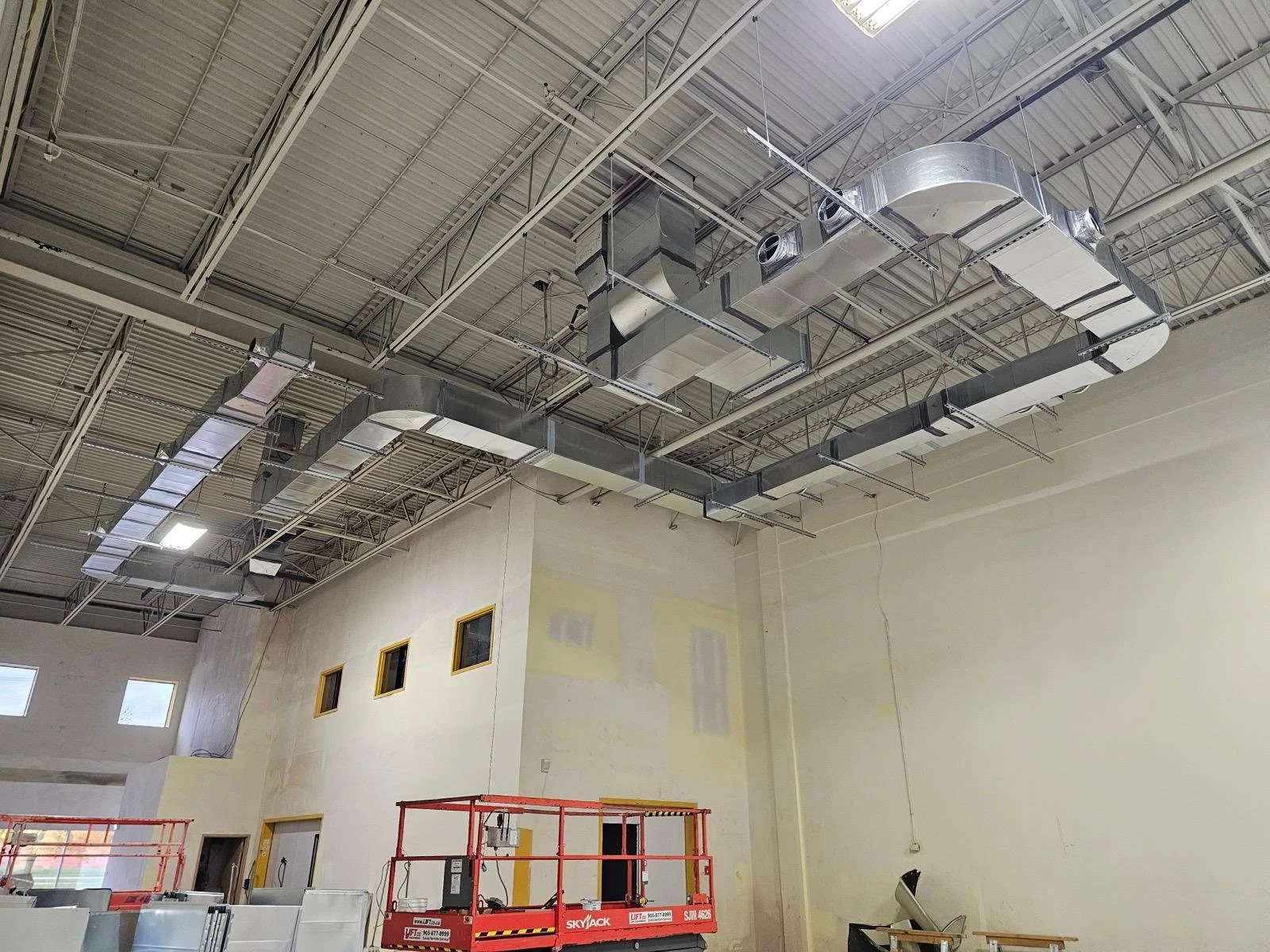 Indoor construction site with exposed ductwork on the ceiling, scaffolding, and unfinished walls.