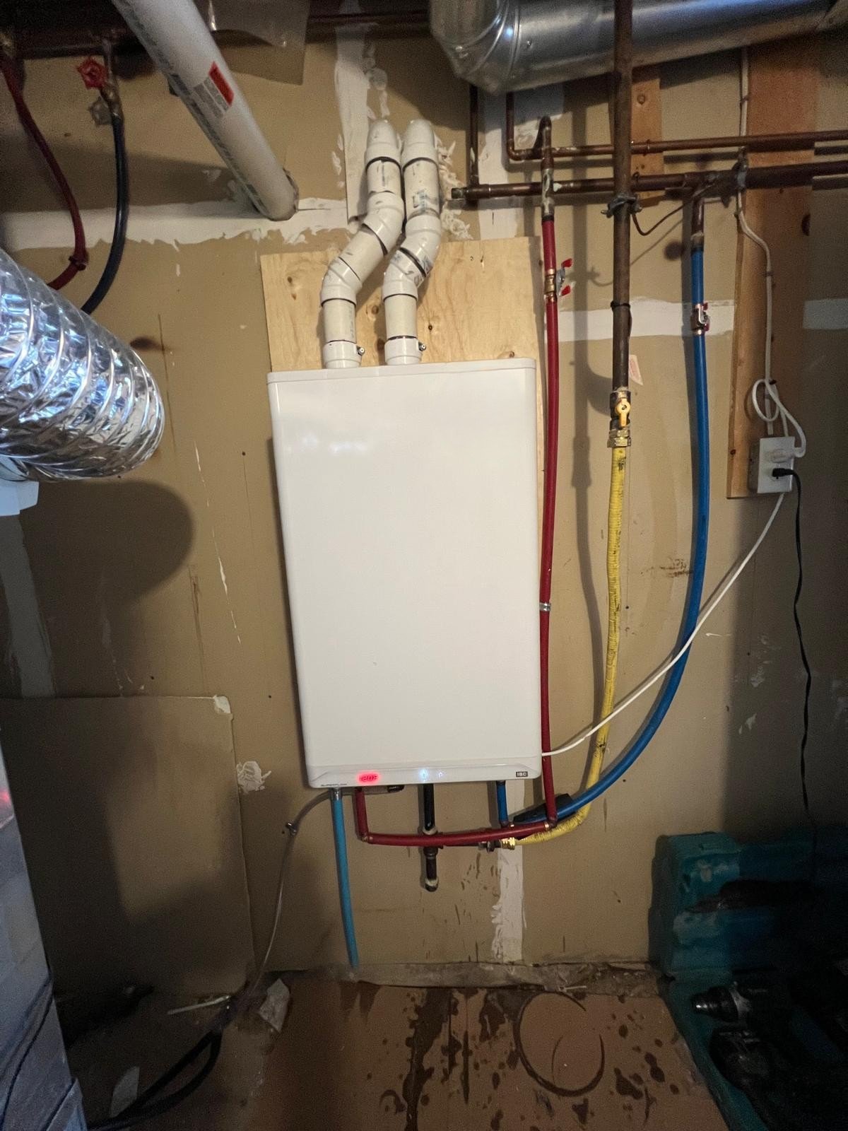 A utility room with a wall-mounted water heater, pipes, and electrical wiring.