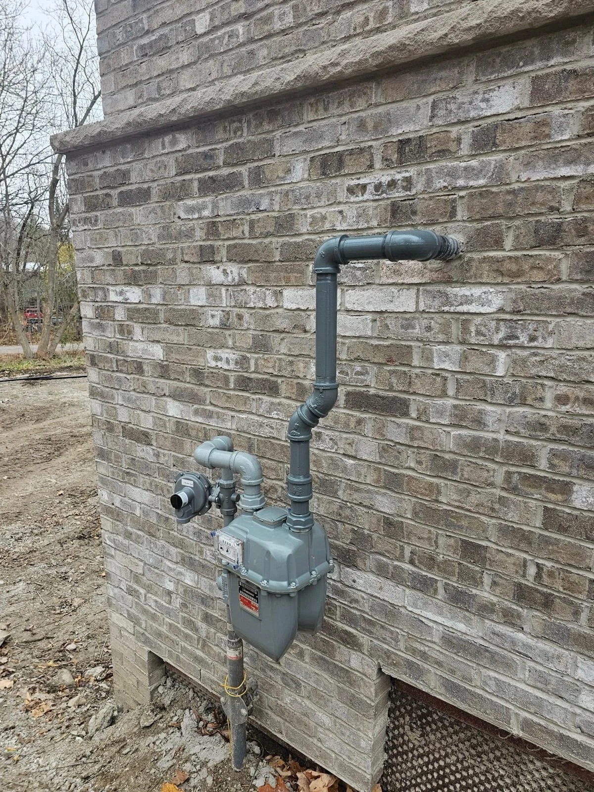 Natural gas meter and pipes attached to the side of a brick building.