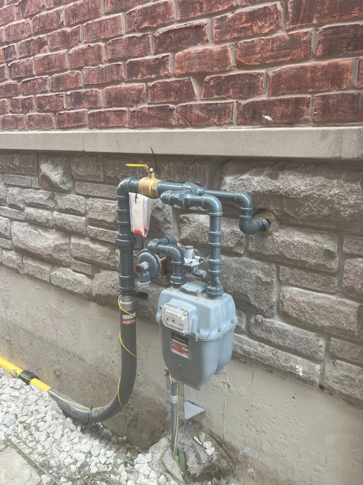 Natural gas meter and piping outside a building with brick and stone exterior walls.