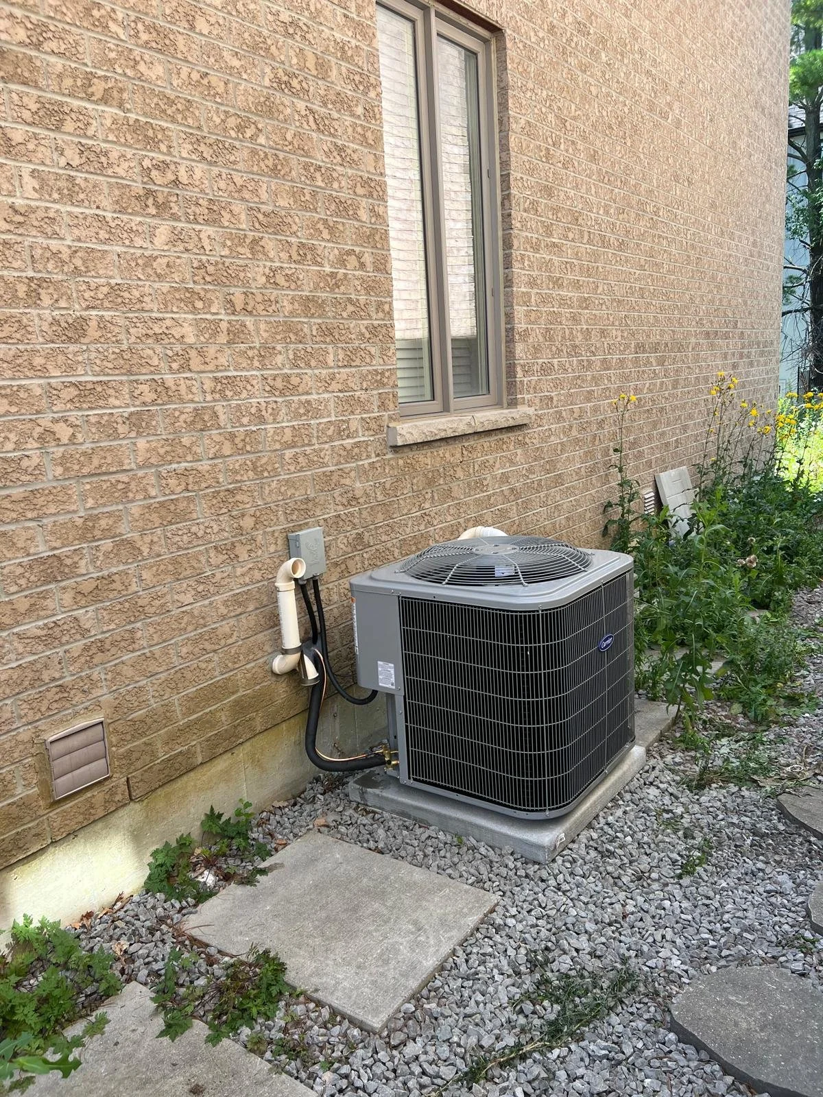 Exterior view of a brick house with an air conditioning unit installed outside, surrounded by gravel and plants.