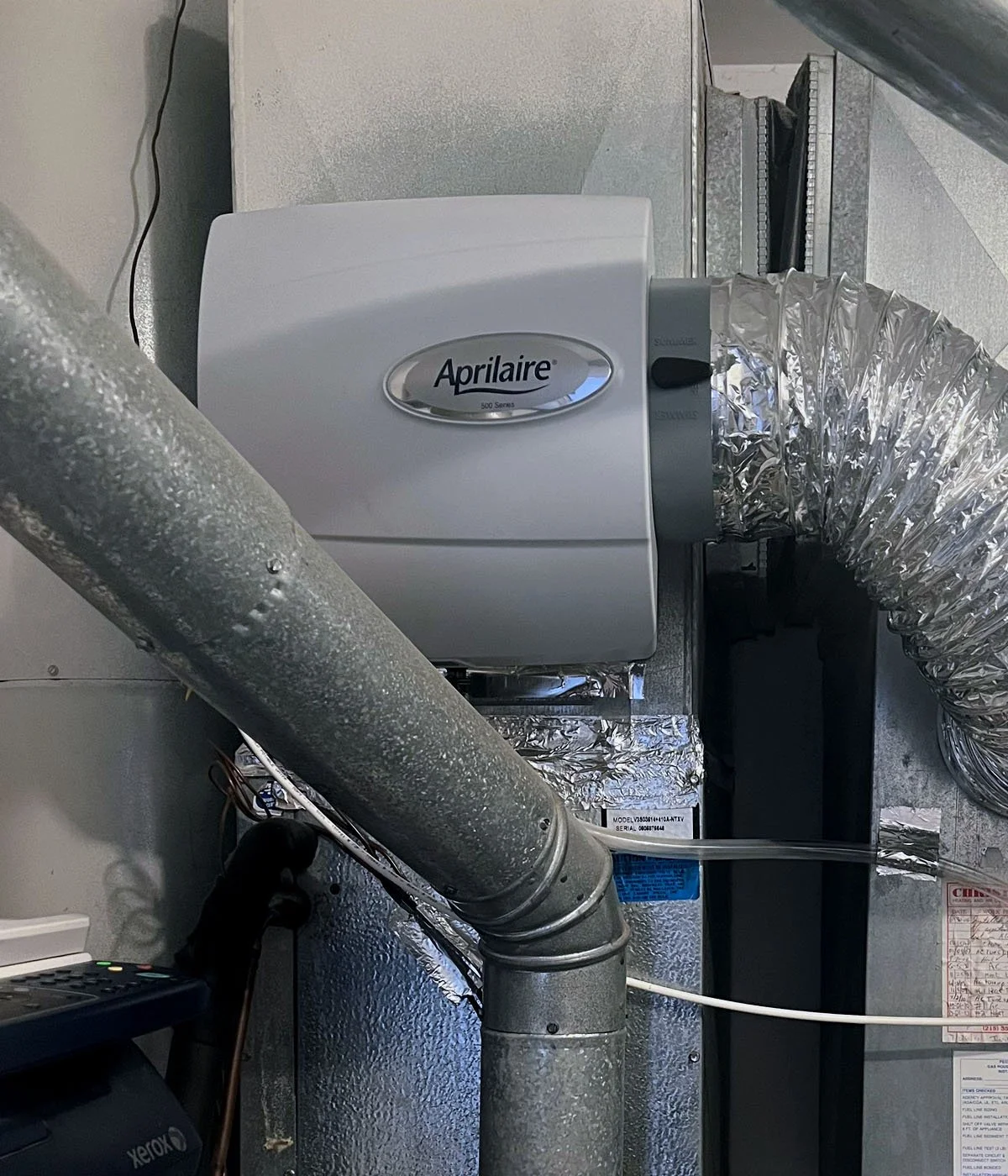Image of an Aprilaire 500 Series humidifier attached to a ventilation duct system in a mechanical room.