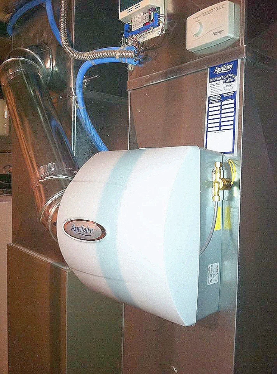 A white water heater labeled 'Aqueaire' connected to plumbing and electrical components in a utility room.