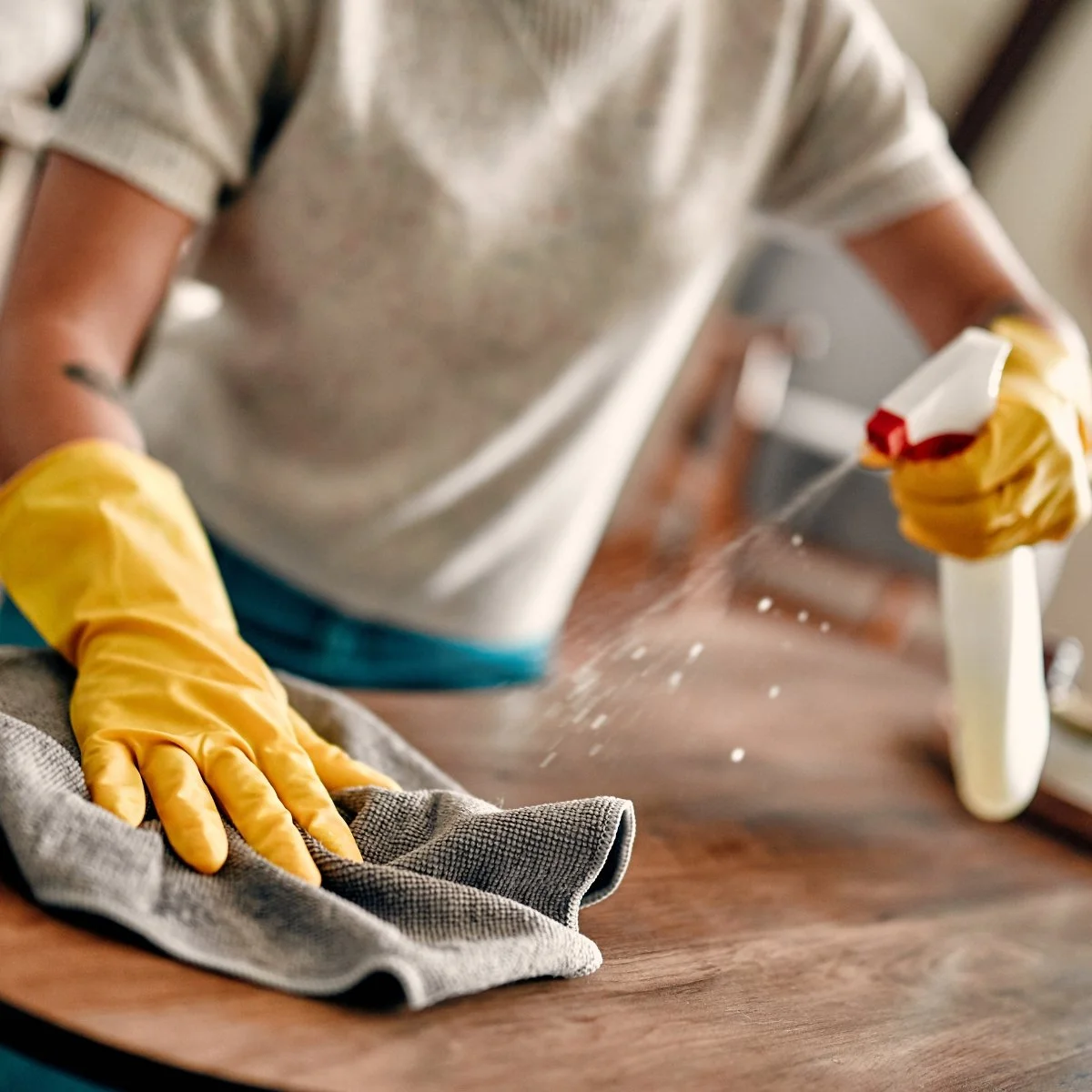 Person wearing yellow rubber gloves cleaning a wooden kitchen countertop with a gray cloth.