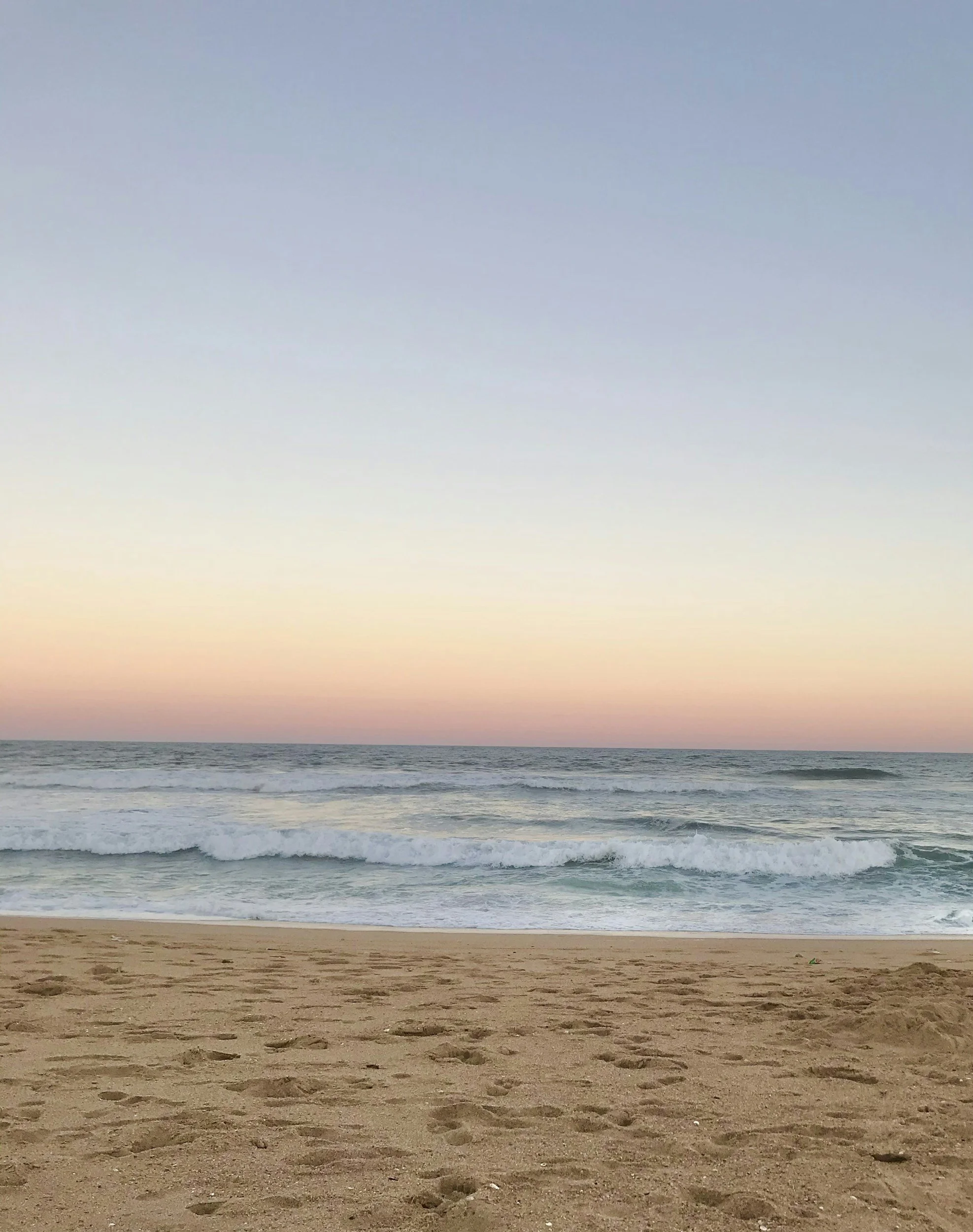 A peaceful beach scene at sunset with sandy shore, gentle waves, and a pastel-colored sky.