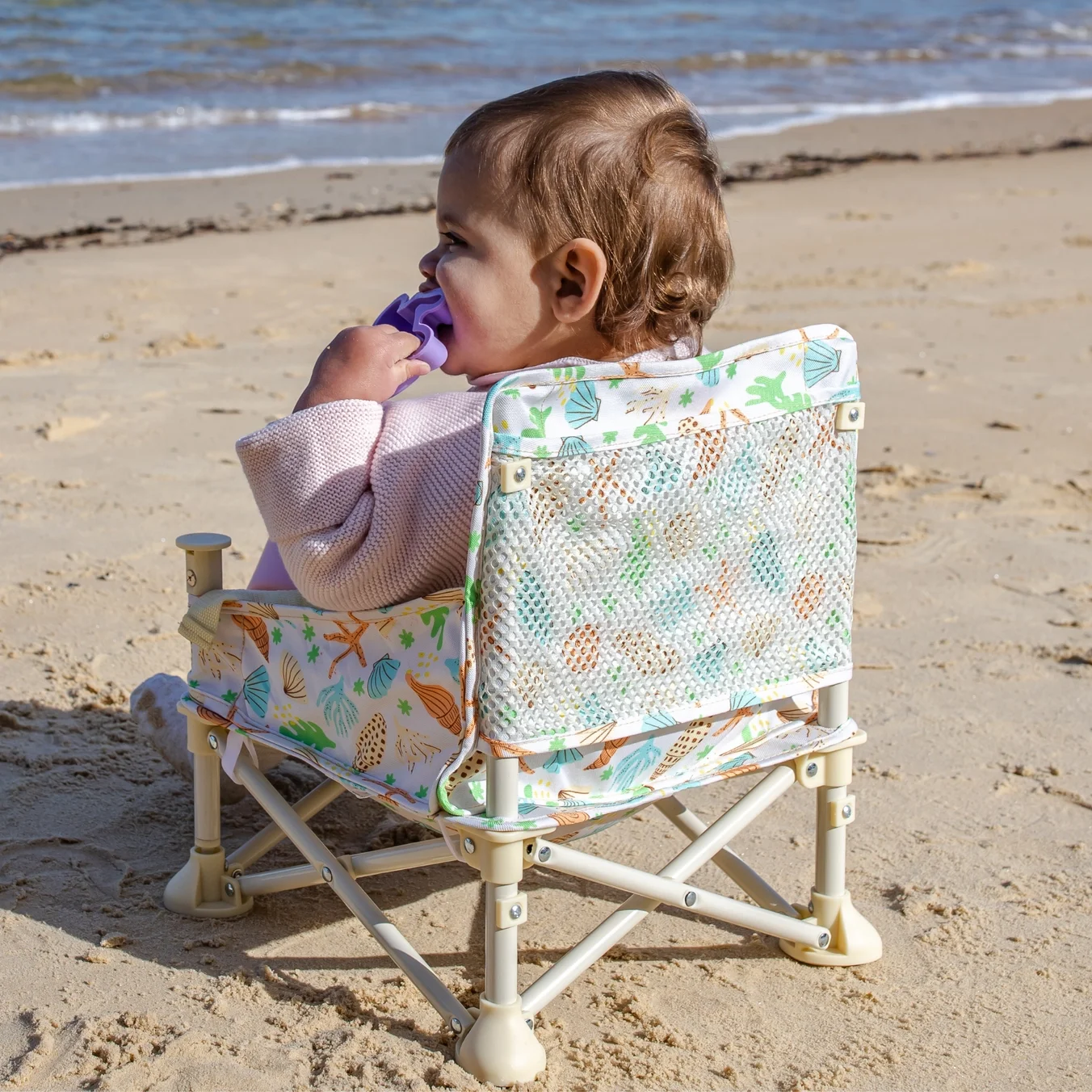 Colorful plastic sand toys on a sandy beach, including a blue shovel, a yellow sieve, a white bucket, and two green bunny-shaped containers, some filled with sand.