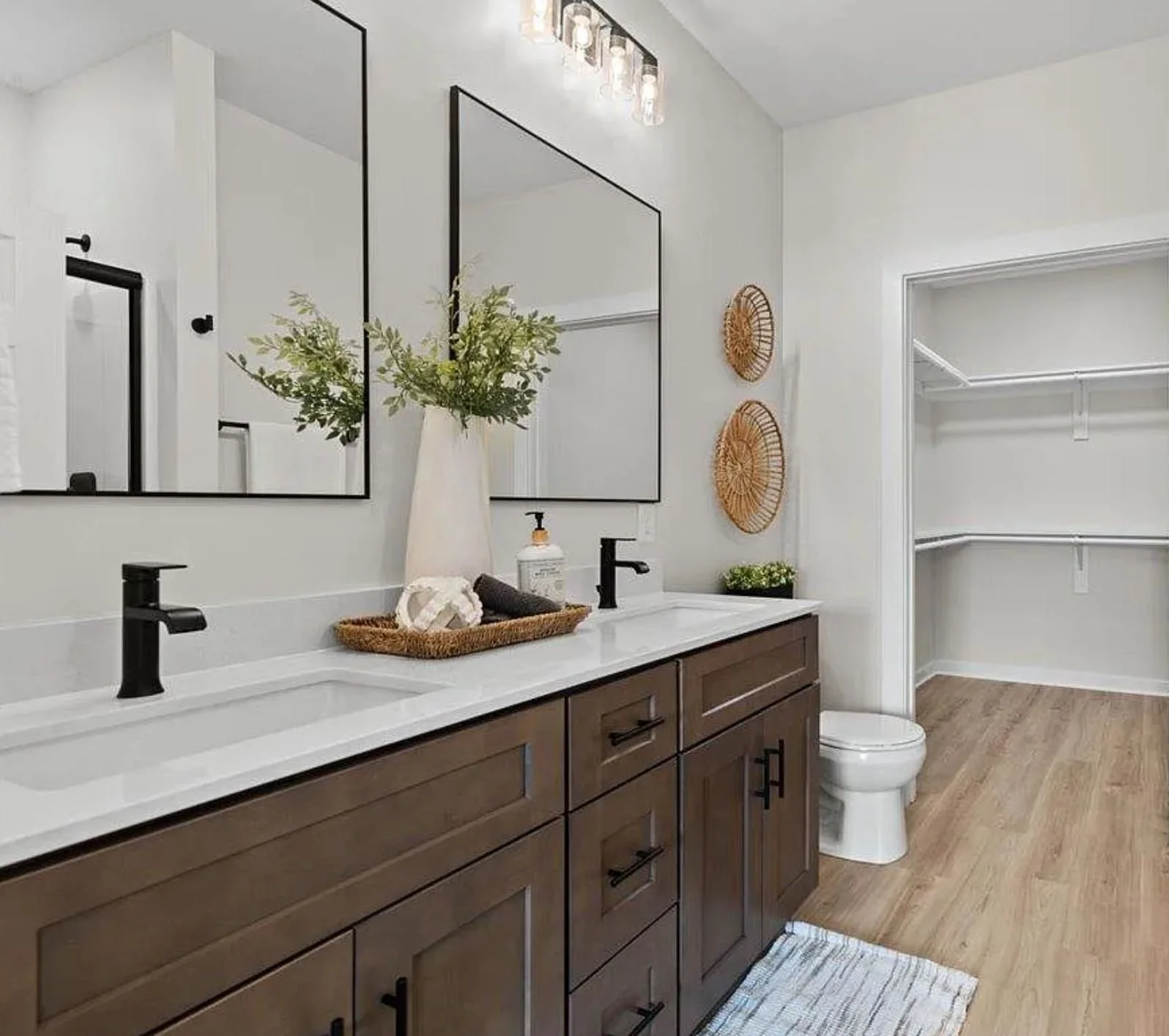A bathroom with a double sink vanity, black fixtures, large mirrors, and a closet area with built-in shelves.