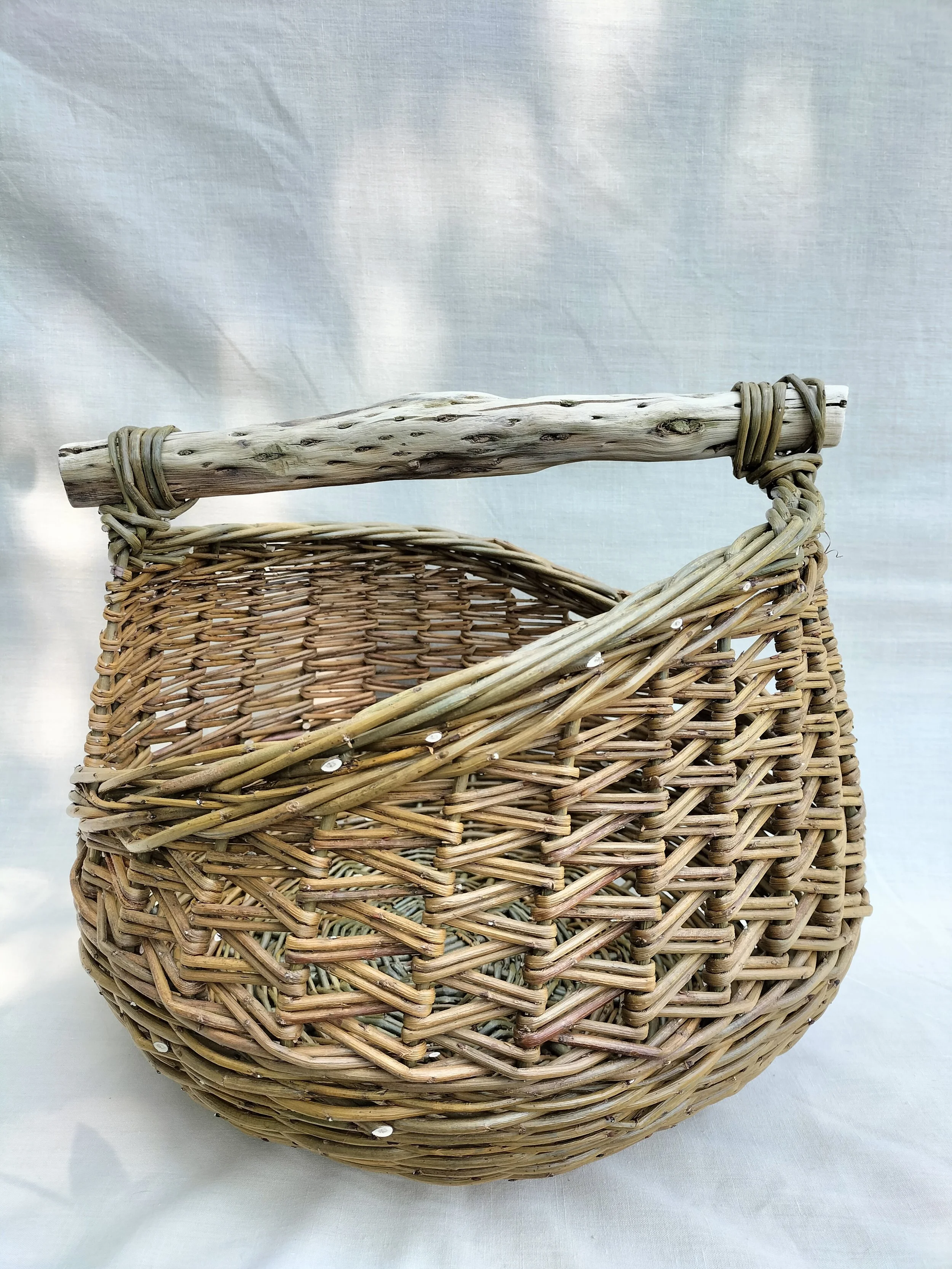 A woven wicker basket with a wooden handle against a plain background.