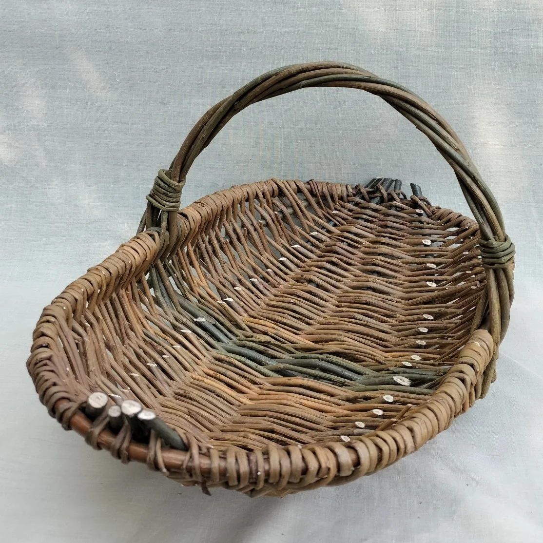 A woven wicker basket with a handle, placed on a white surface.