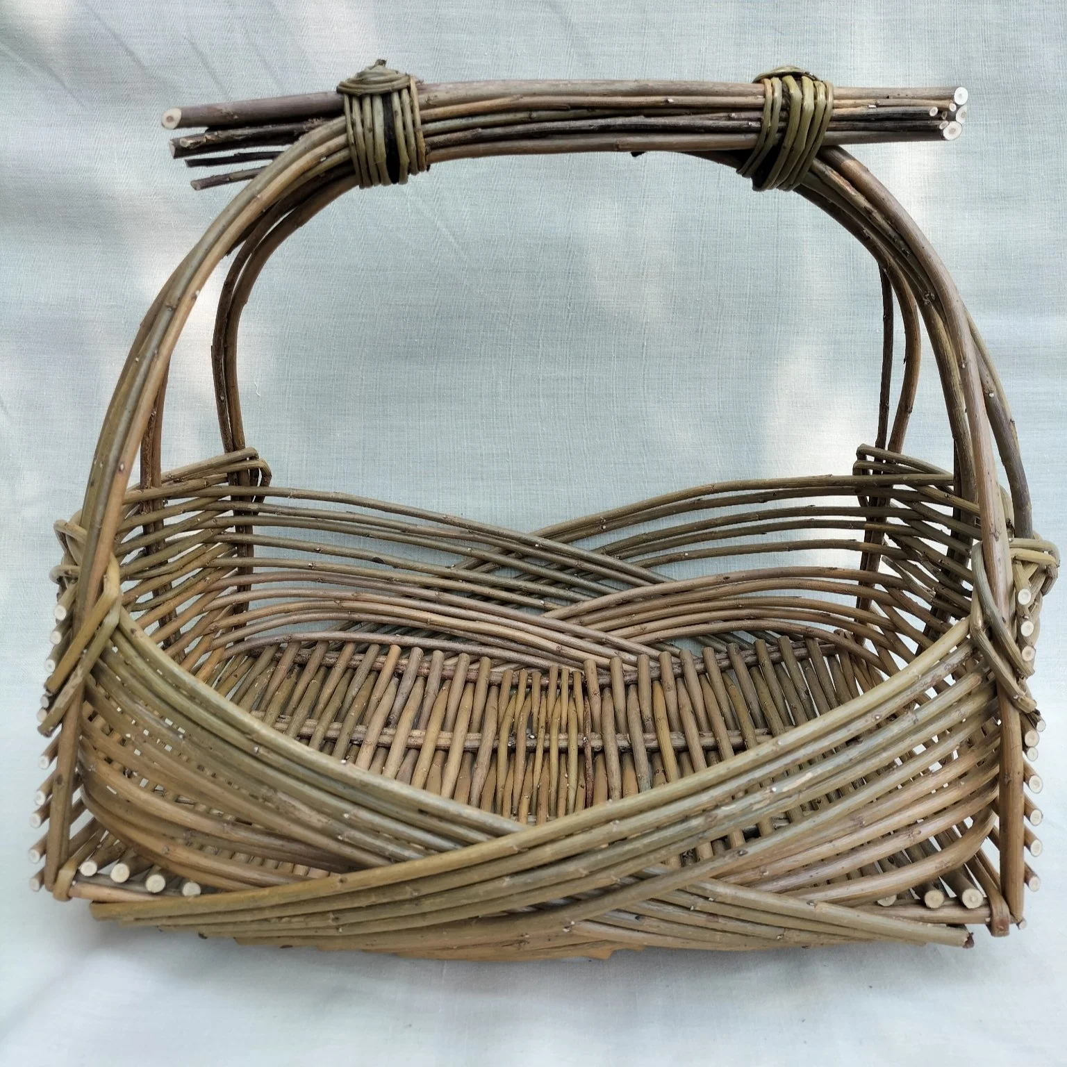 A woven wicker basket with a rounded handle and a detailed intertwined design.