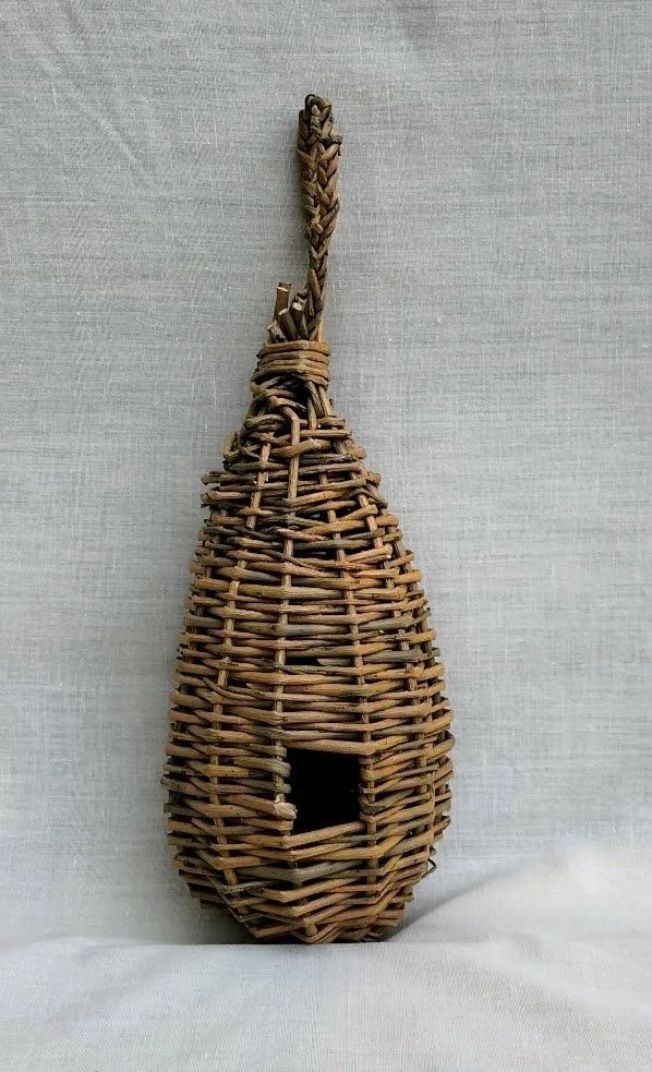 A woven wicker birdhouse in the shape of a guitar, hanging against a light gray background.