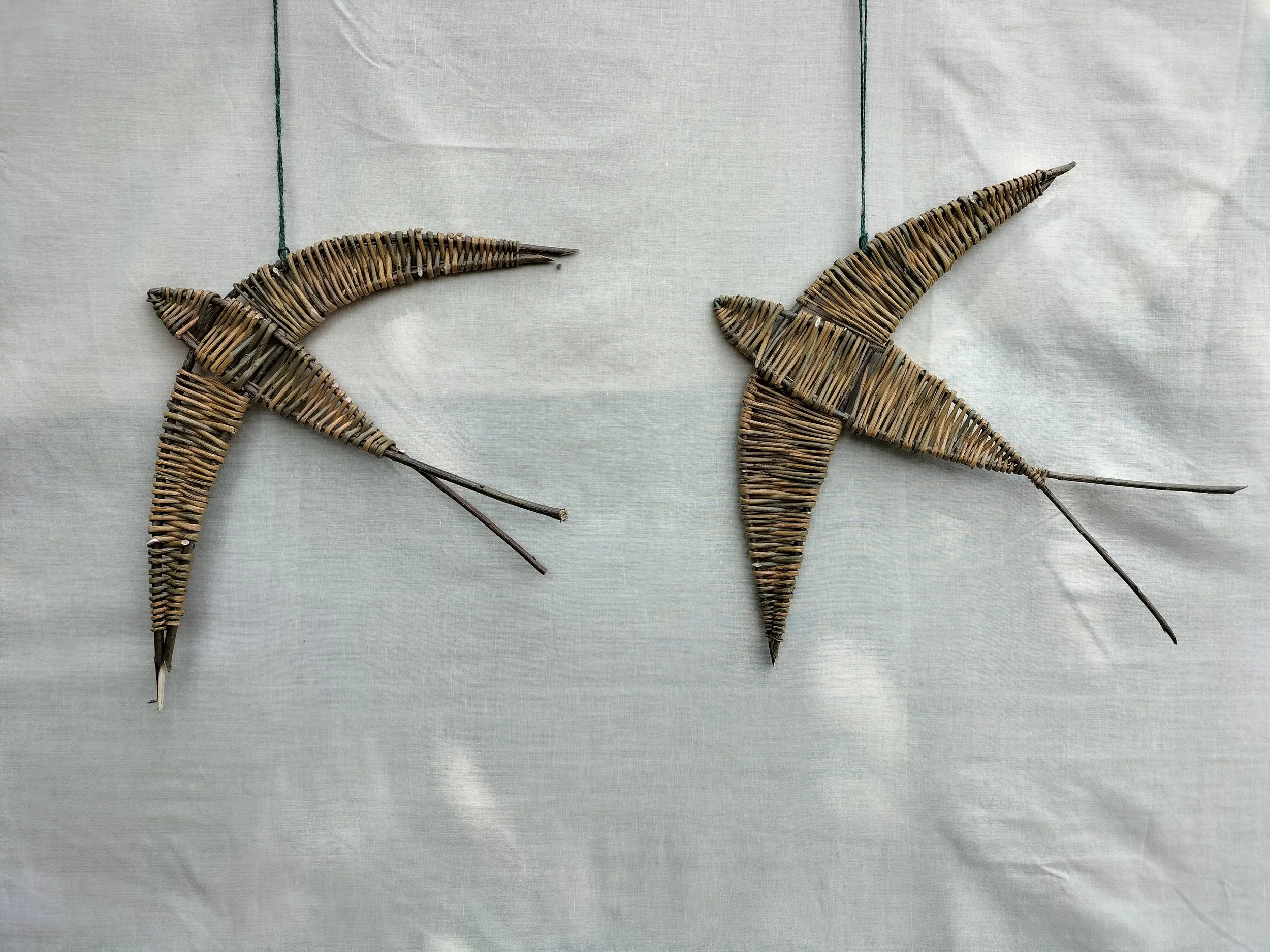 Two decorative star-shaped figures made from woven natural materials, hanging on a white fabric background.