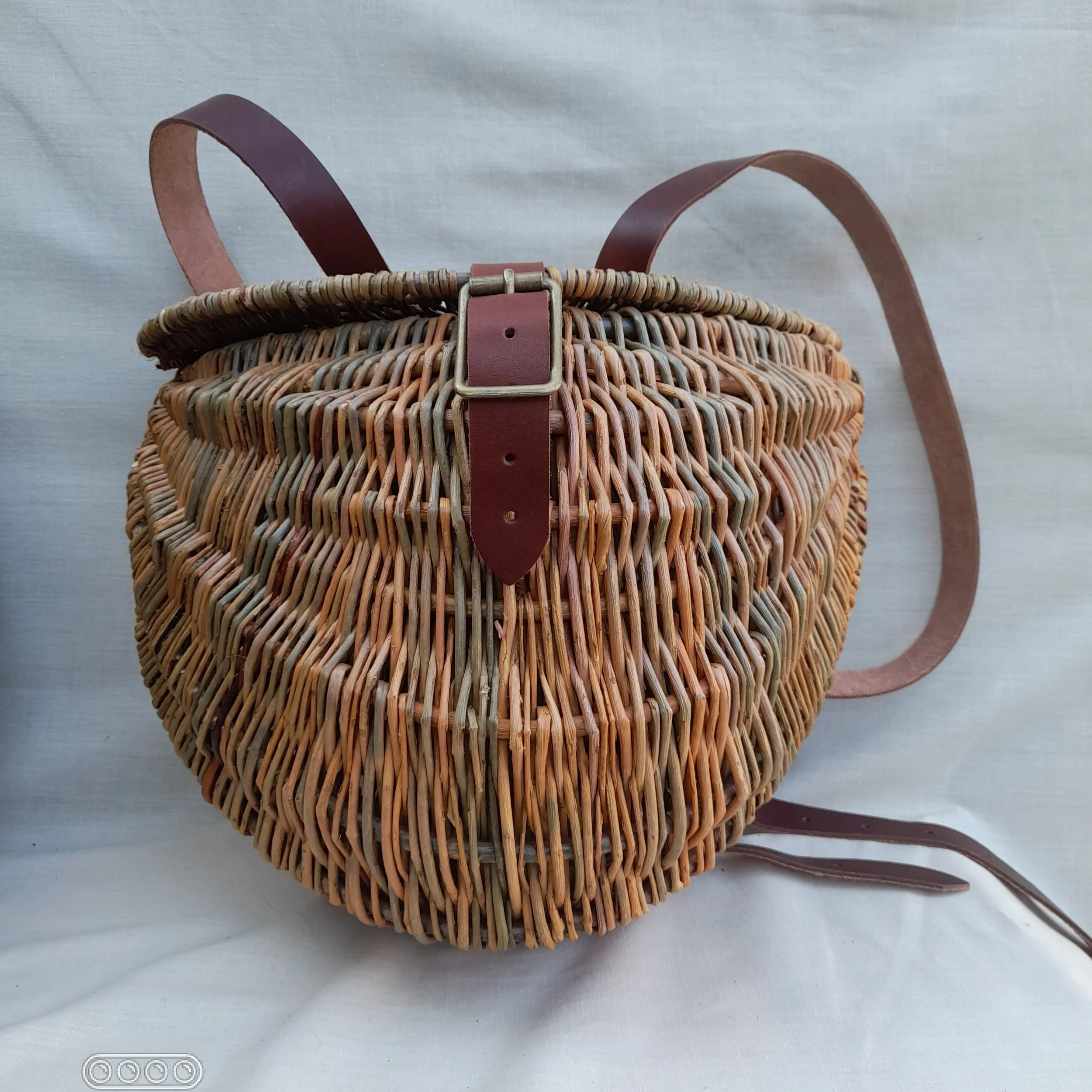 A woven basket with leather straps and a buckle, set against a plain background.