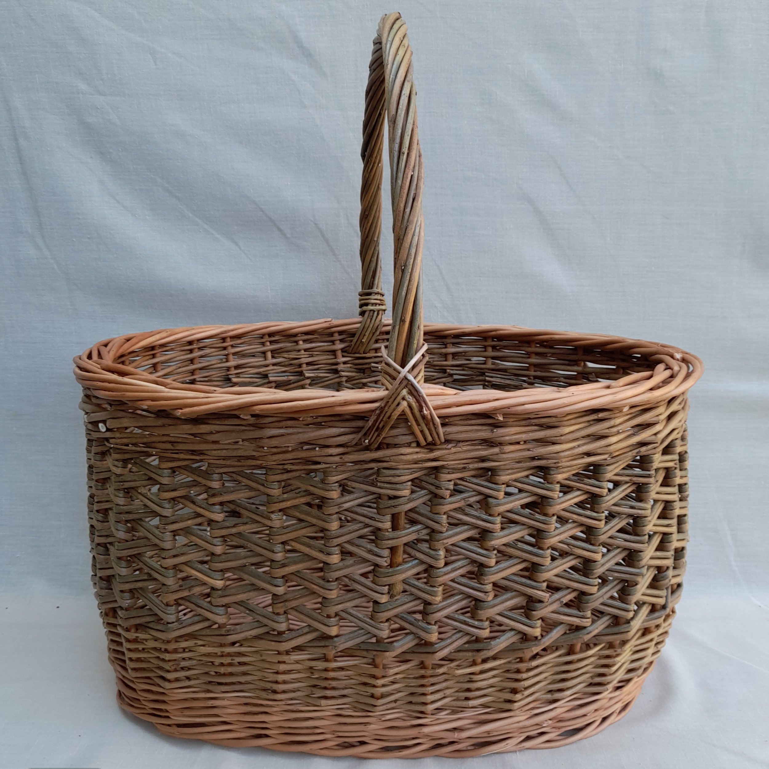 Handwoven wicker basket with a handle, set against a plain background.