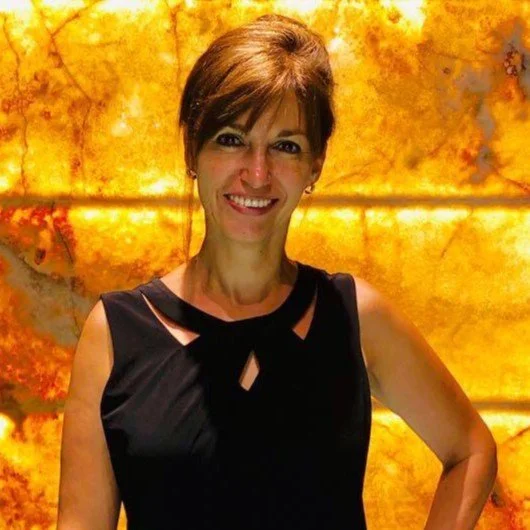 Mujer sonriendo frente a un fondo de piedra con iluminación cálida.