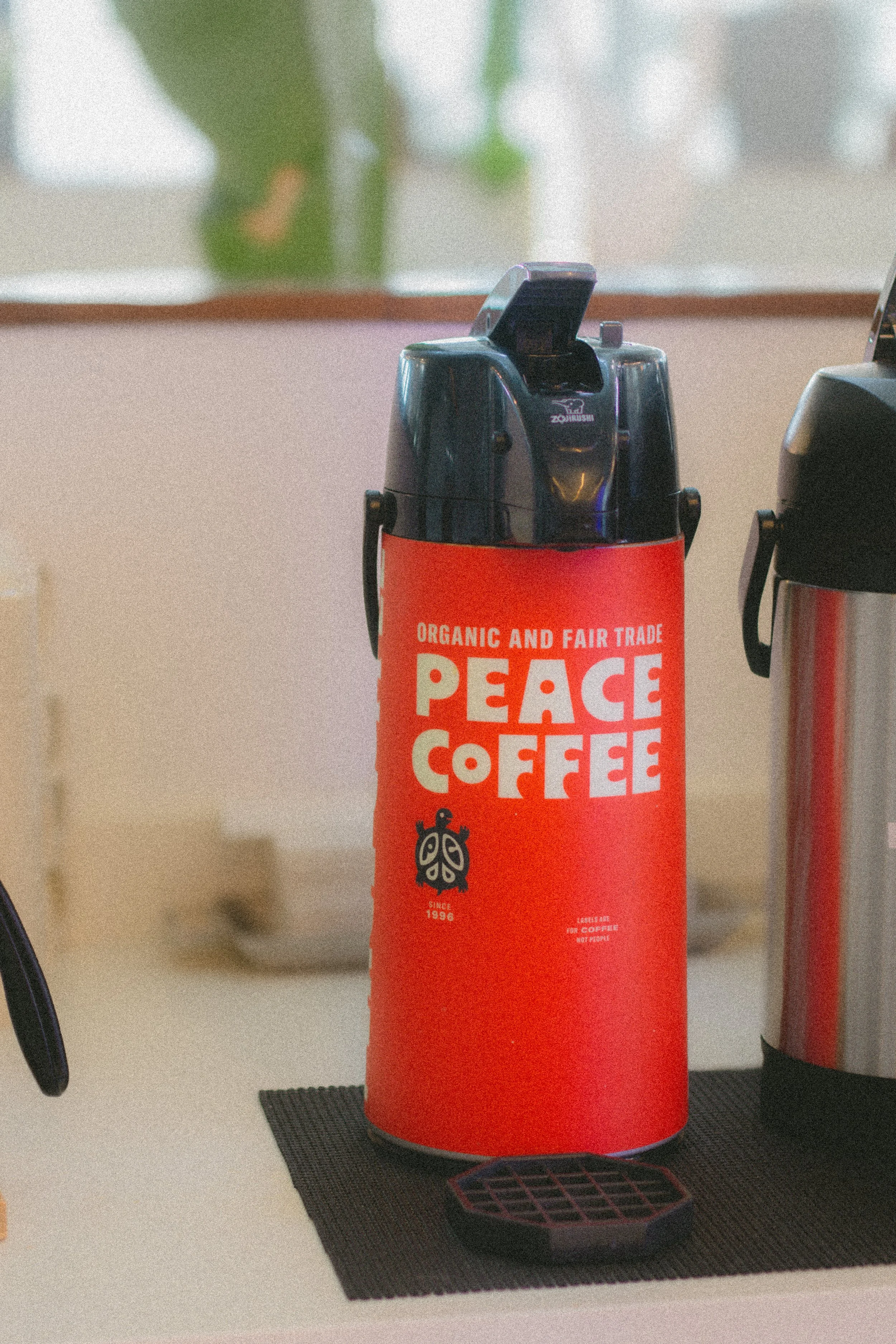 A red coffee thermos with a black lid and a label reading "Peace Coffee" on a black placemat.