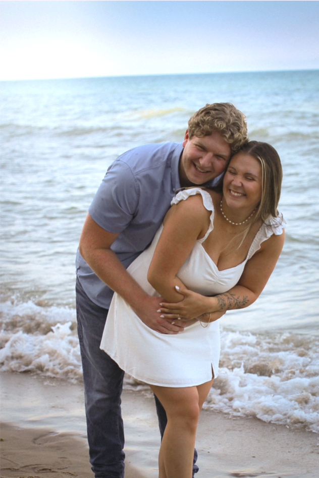 A happy couple hugging on the beach by the ocean, smiling and enjoying the moment.