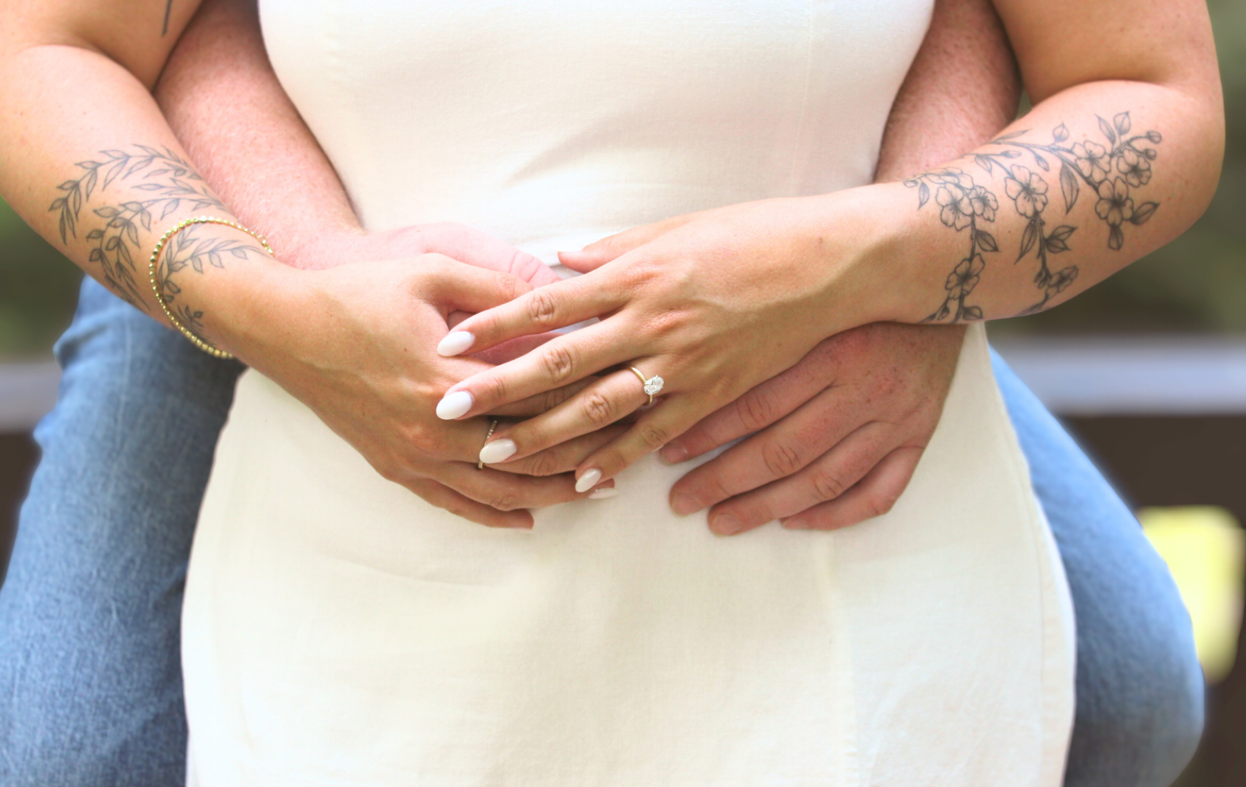 A close-up of an engagement photo, showing tattoos on her arms and a diamond ring on her ring finger.