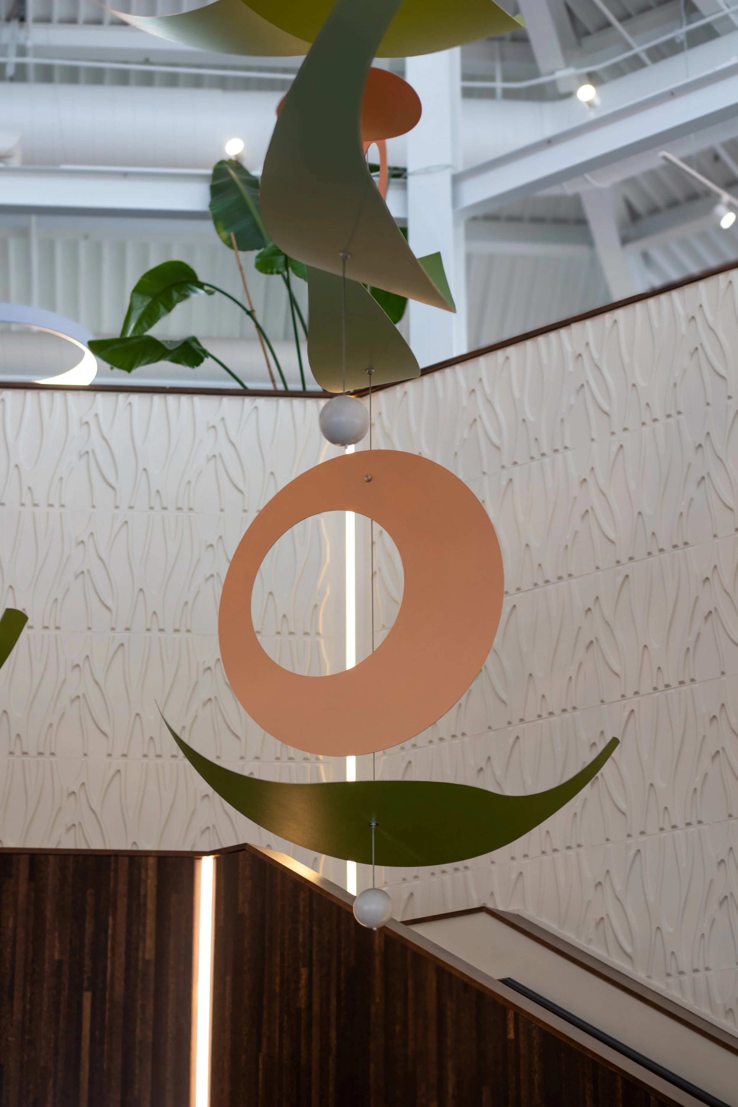 Decorative mobile hanging in a modern interior with white textured walls, green plants, and wooden accents.