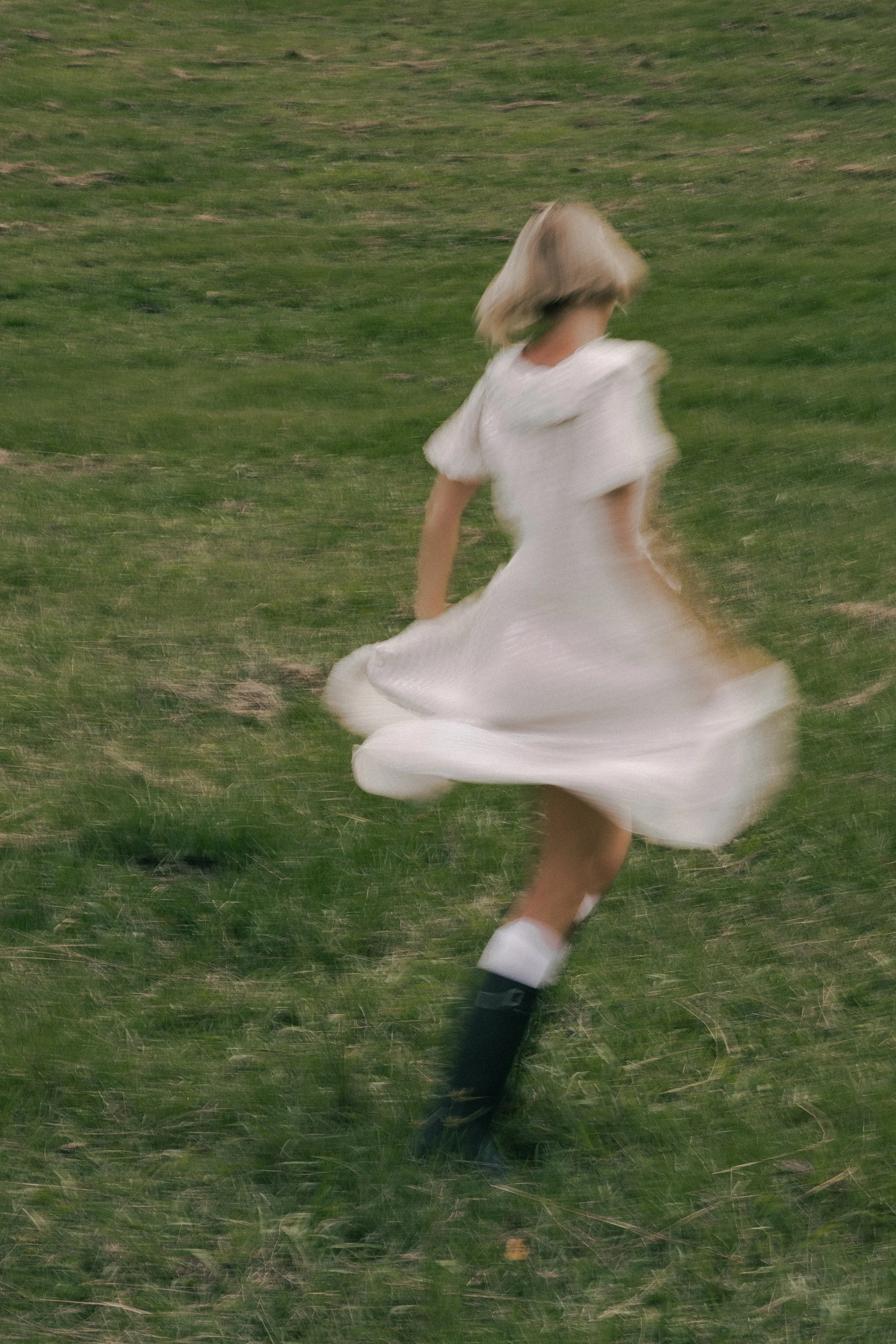 A girl in a white dress running on a grassy field with her hair moving.