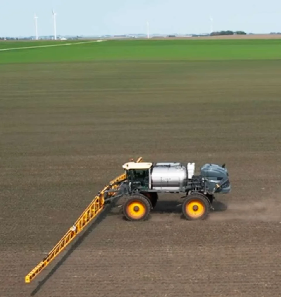 A large agricultural sprayer moving across a farmland field, spraying crops.