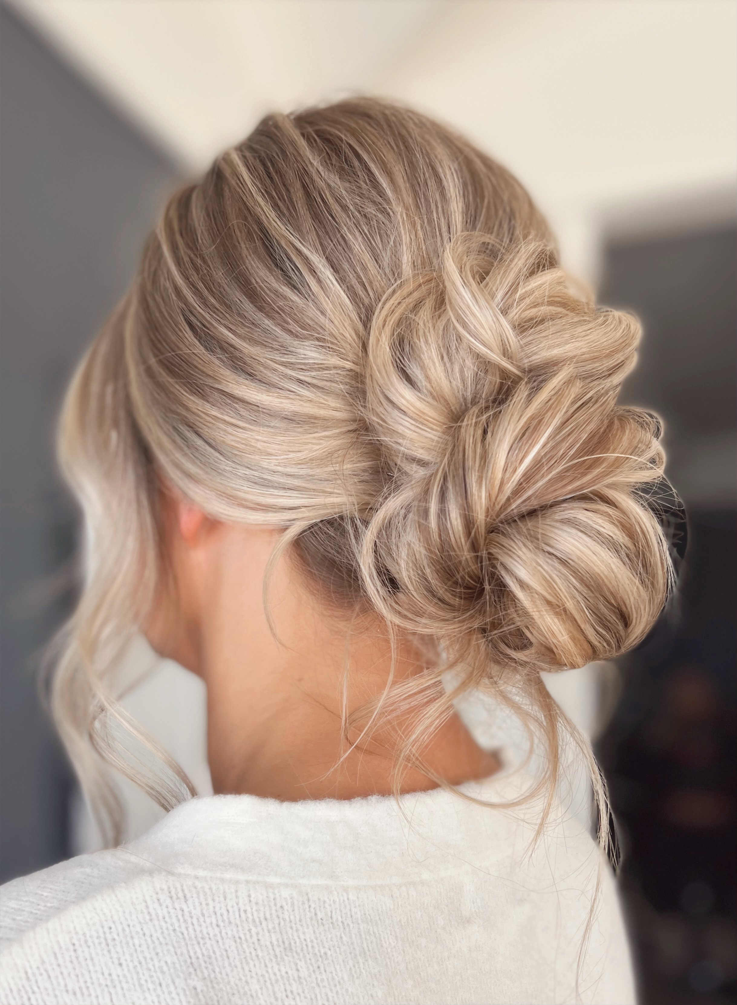 A blonde woman with styled hair in a loose updo with curls and twists.