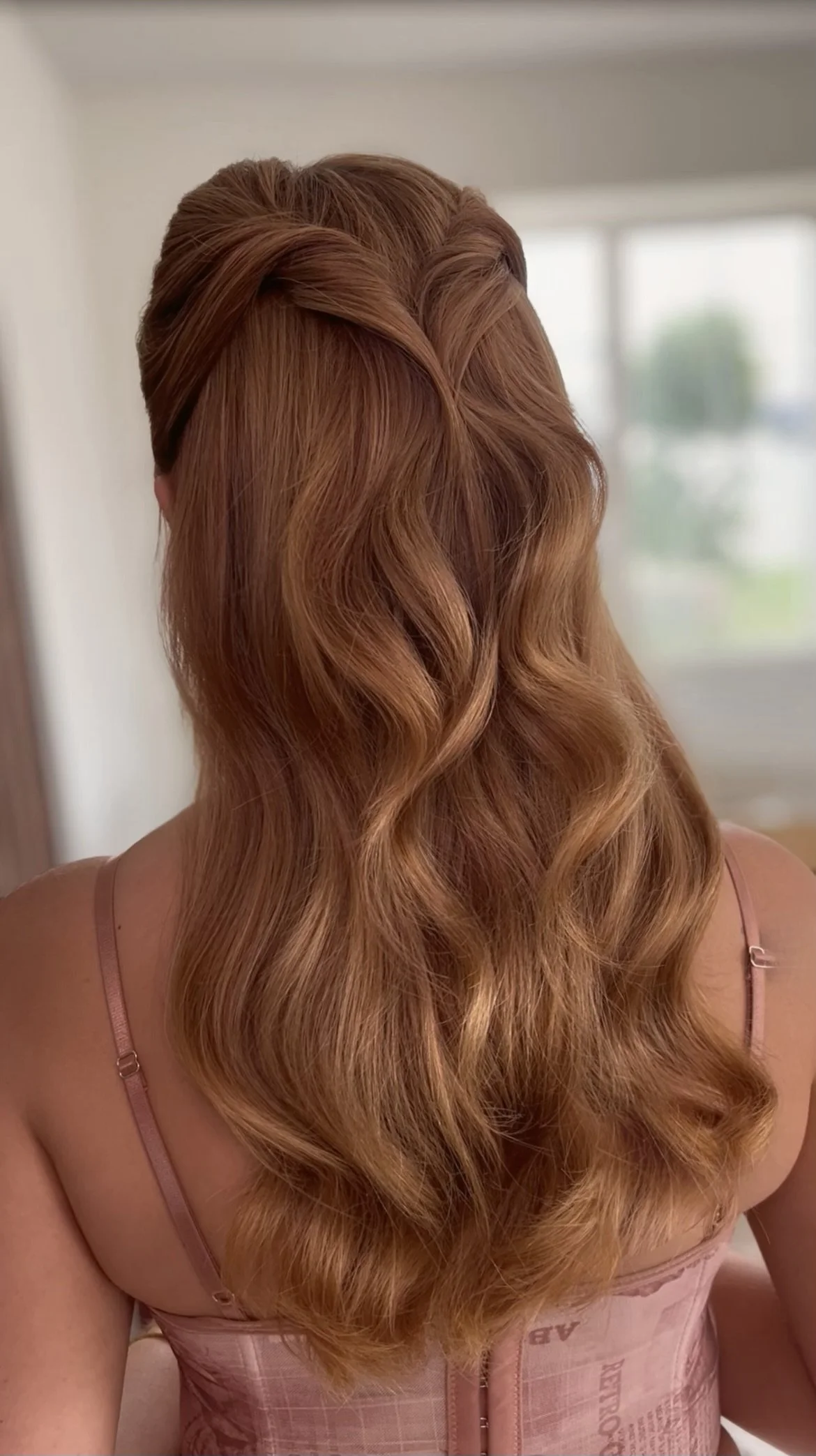 Back view of a woman with long, wavy, auburn hair in a softly lit room.