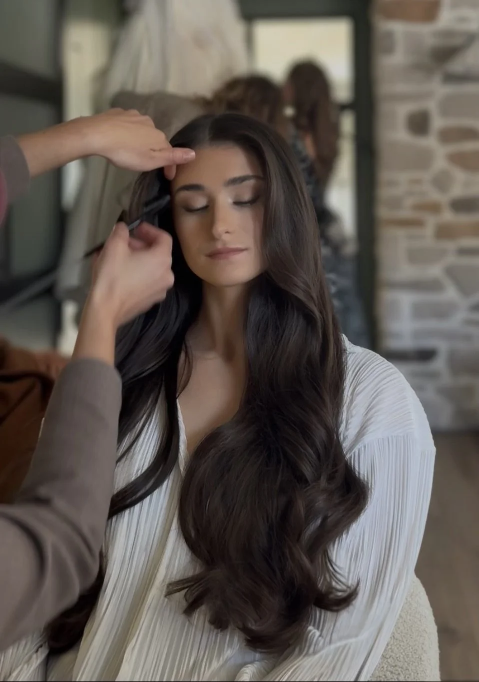 A woman getting her makeup or hair done at a salon, with her eyes closed and long dark hair.