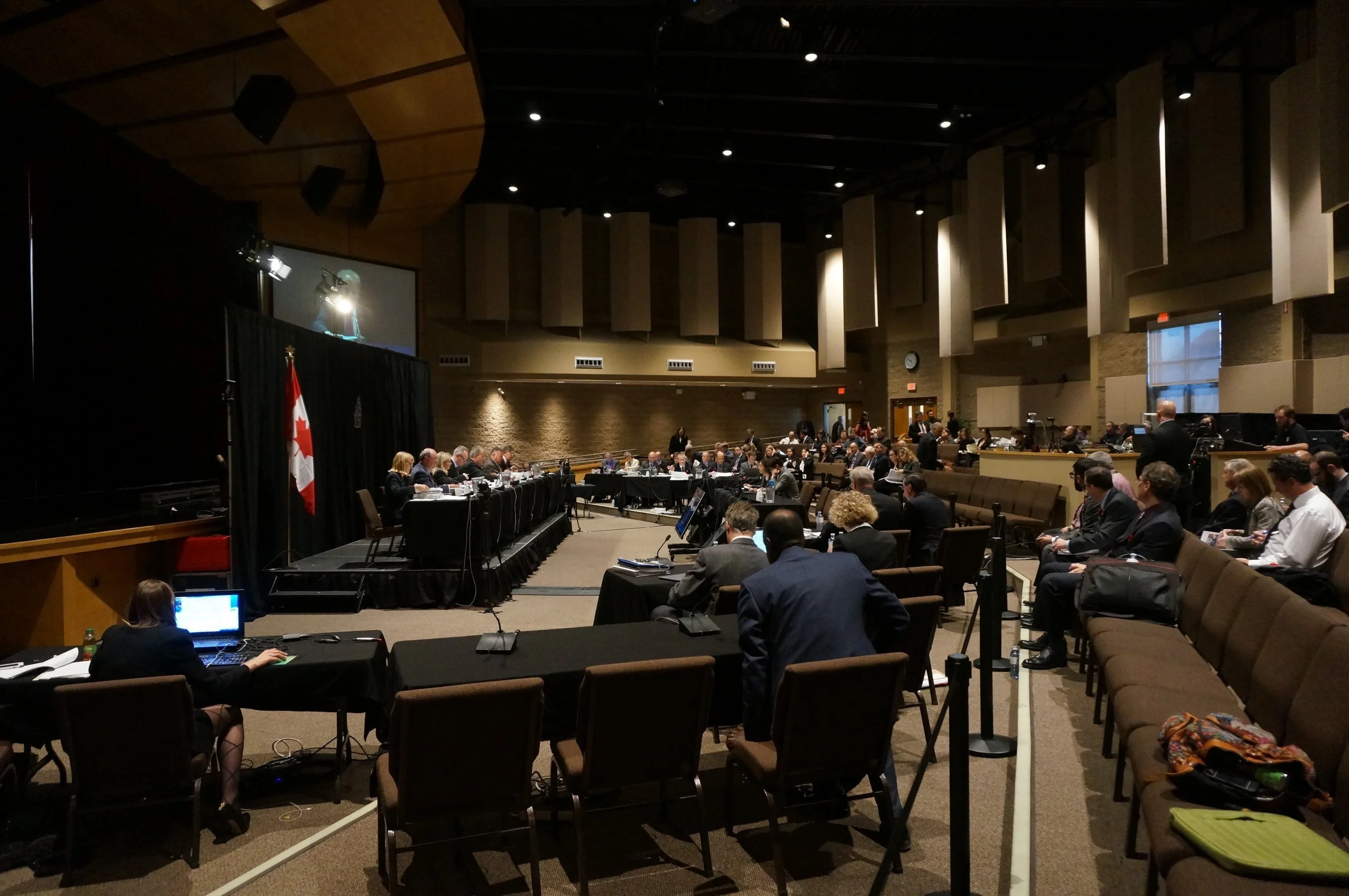  The Commission sitting on the raised stage to the left. OPG representatives, intervenor tables and CNSC staff located in the cordoned off area facing the Commission.&nbsp;(Photo by Lake Ontario Waterkeeper) 