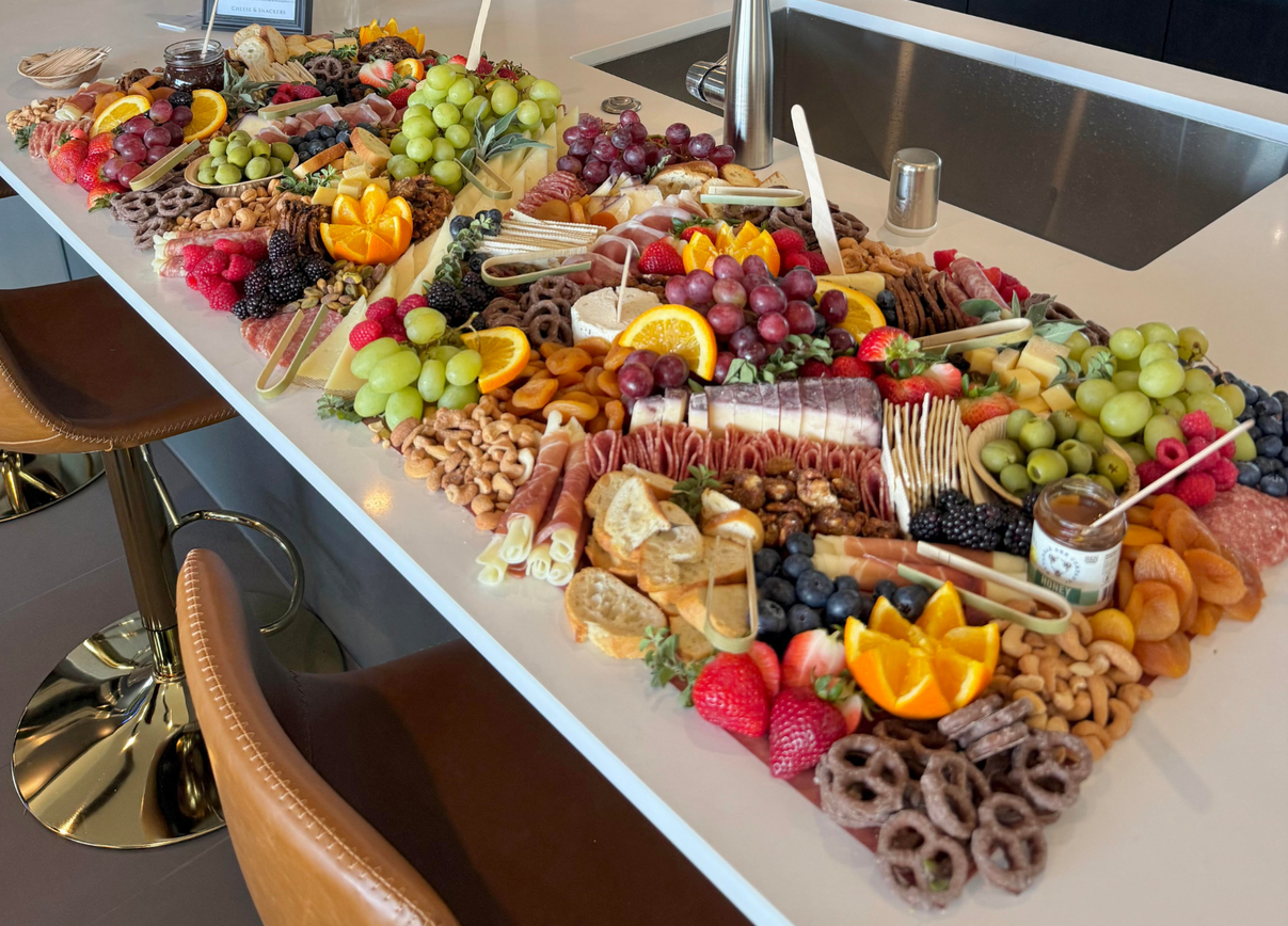 A large charcuterie board on a kitchen island with assorted fruits, cheeses, crackers, nuts, meats, and spreads.