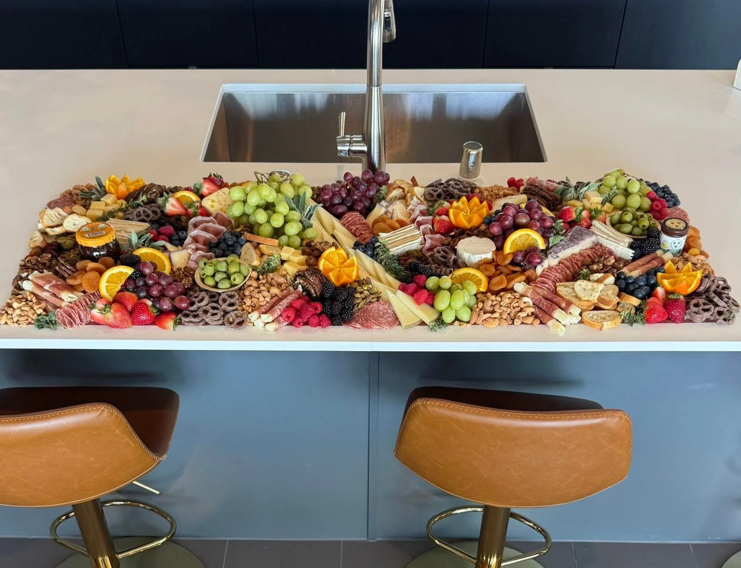 Charcuterie board with assorted cheeses, fruits, nuts, meats, and snacks on a kitchen island counter.
