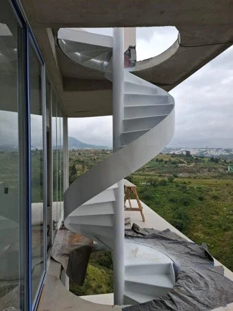 Escalera de caracol, de metal blanca en un balcón con vista panorámica de campo y ciudad. Escalera metálica