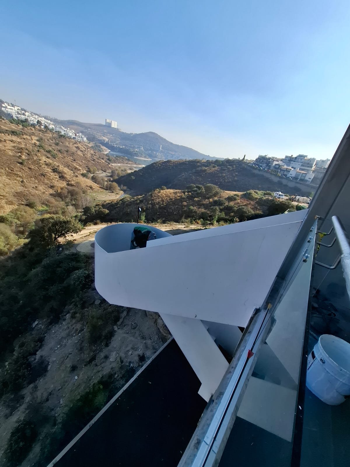 Una estructura moderna en construcción con vista panorámica a colinas y edificios en un entorno natural y urbano.
