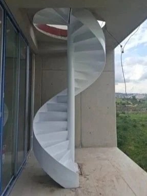Escalera de caracol blanca en un balcón con vista al campo y al cielo