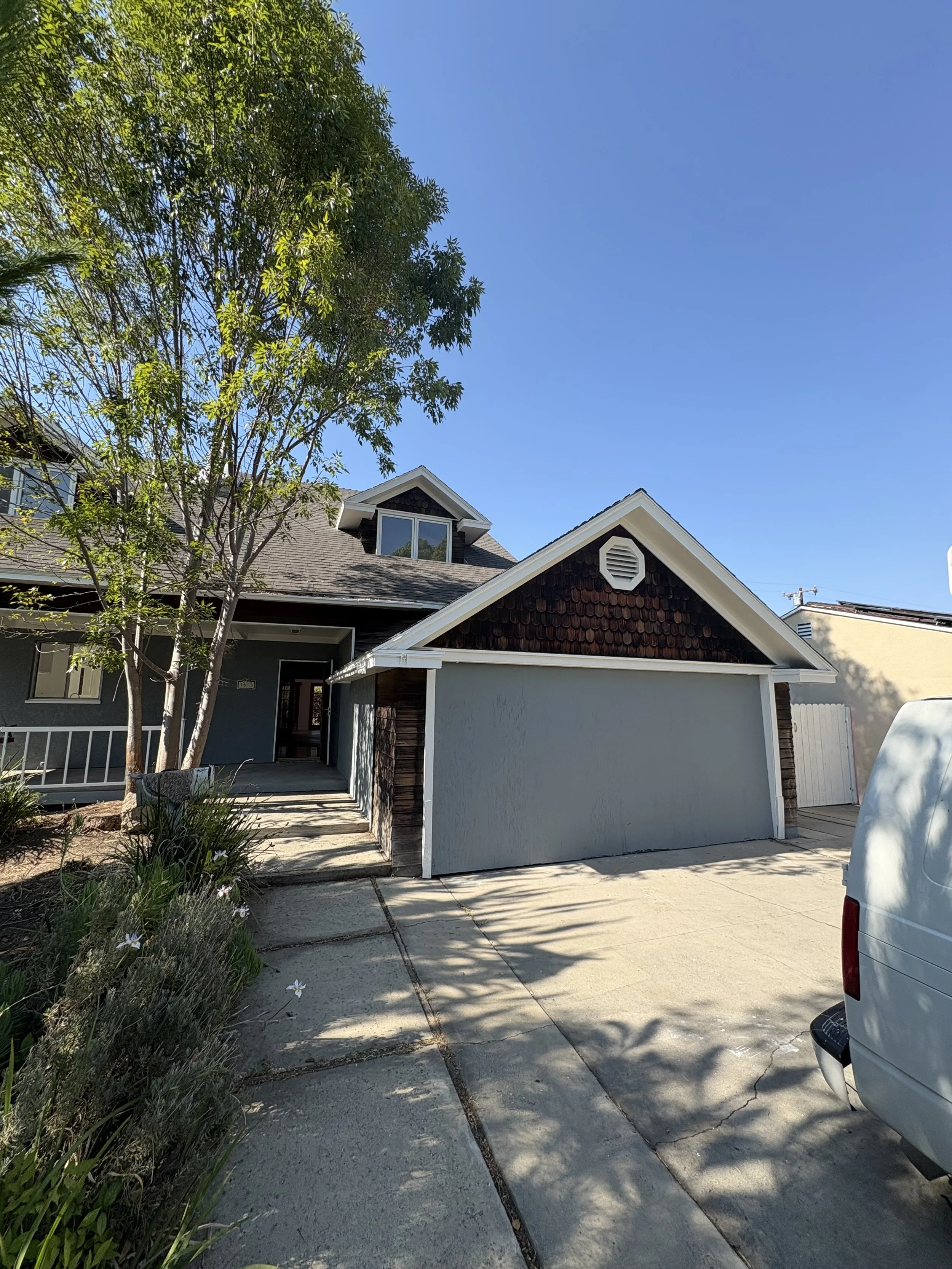 Front view of a house with a driveway, garage door, trees, and clear blue sky.