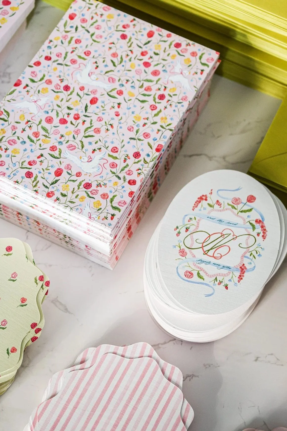 A stack of floral patterned coasters and a box of stationery with a similar floral design, featuring pastel colors and elegant script.