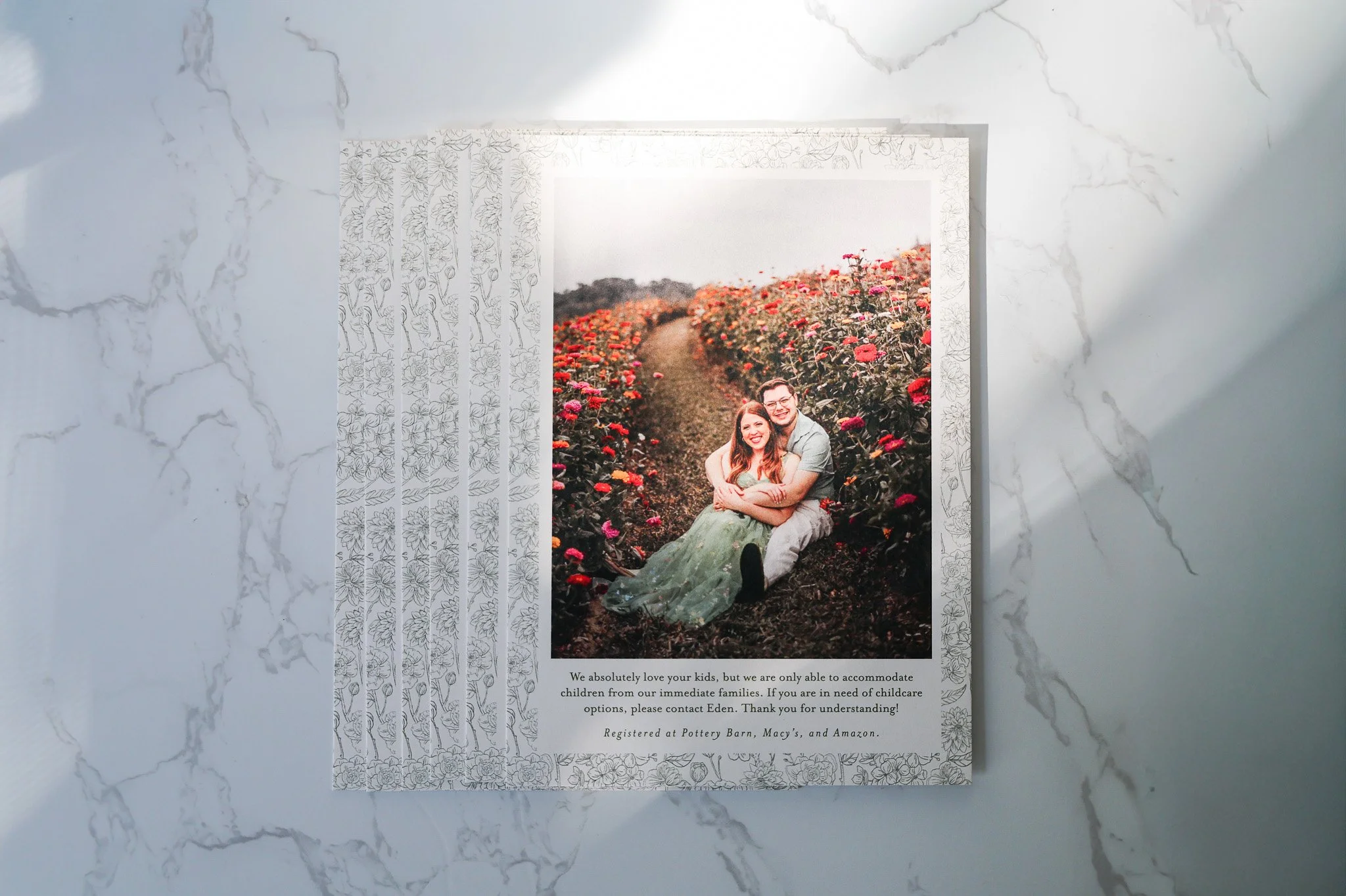 A wedding or engagement photo of a smiling couple sitting in a flower field, with a white and gray marble background, and printed text below the image about child care options at Pottery Barn, Macy's, and Amazon.
