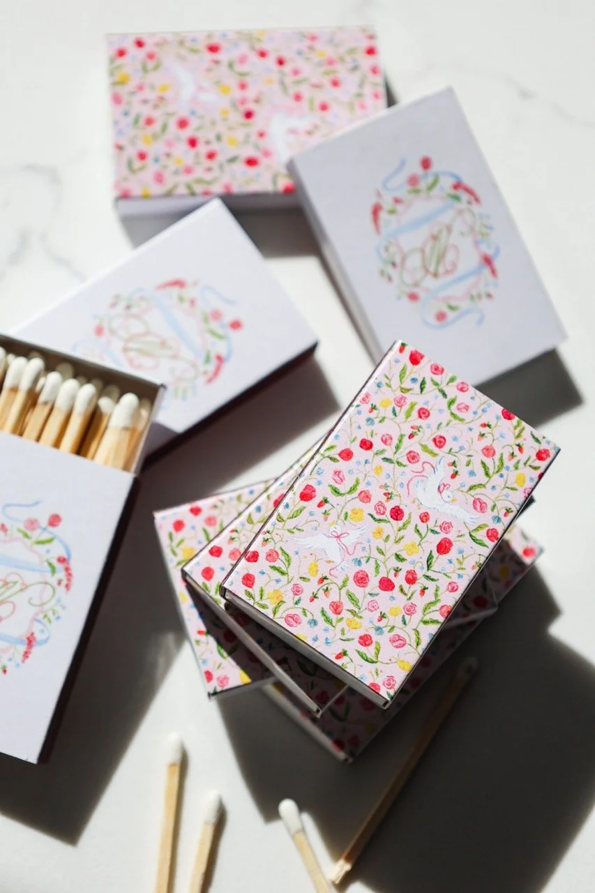 Whimsical wedding matchboxes featuring a monogram and artwork with a floral pattern and doves