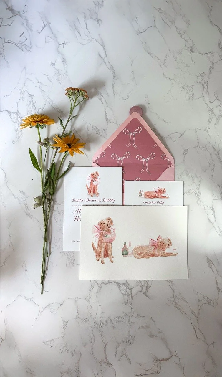 Set of pastel-colored cards with illustrations of dogs, a pink envelope with white bow patterns, and a small bouquet of yellow and tan flowers on a marble surface.