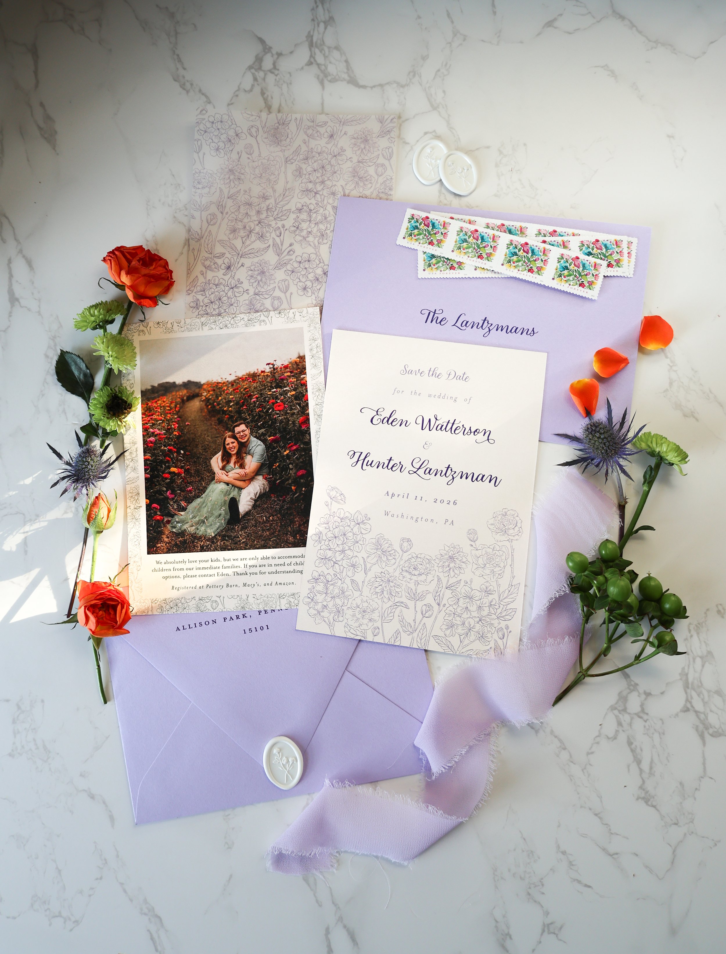 Lavender wedding invitation suite with floral designs, save-the-date card, photo of a couple in a flower field, purple envelope with a wax seal, floral decorations, and scattered flower petals and plants.