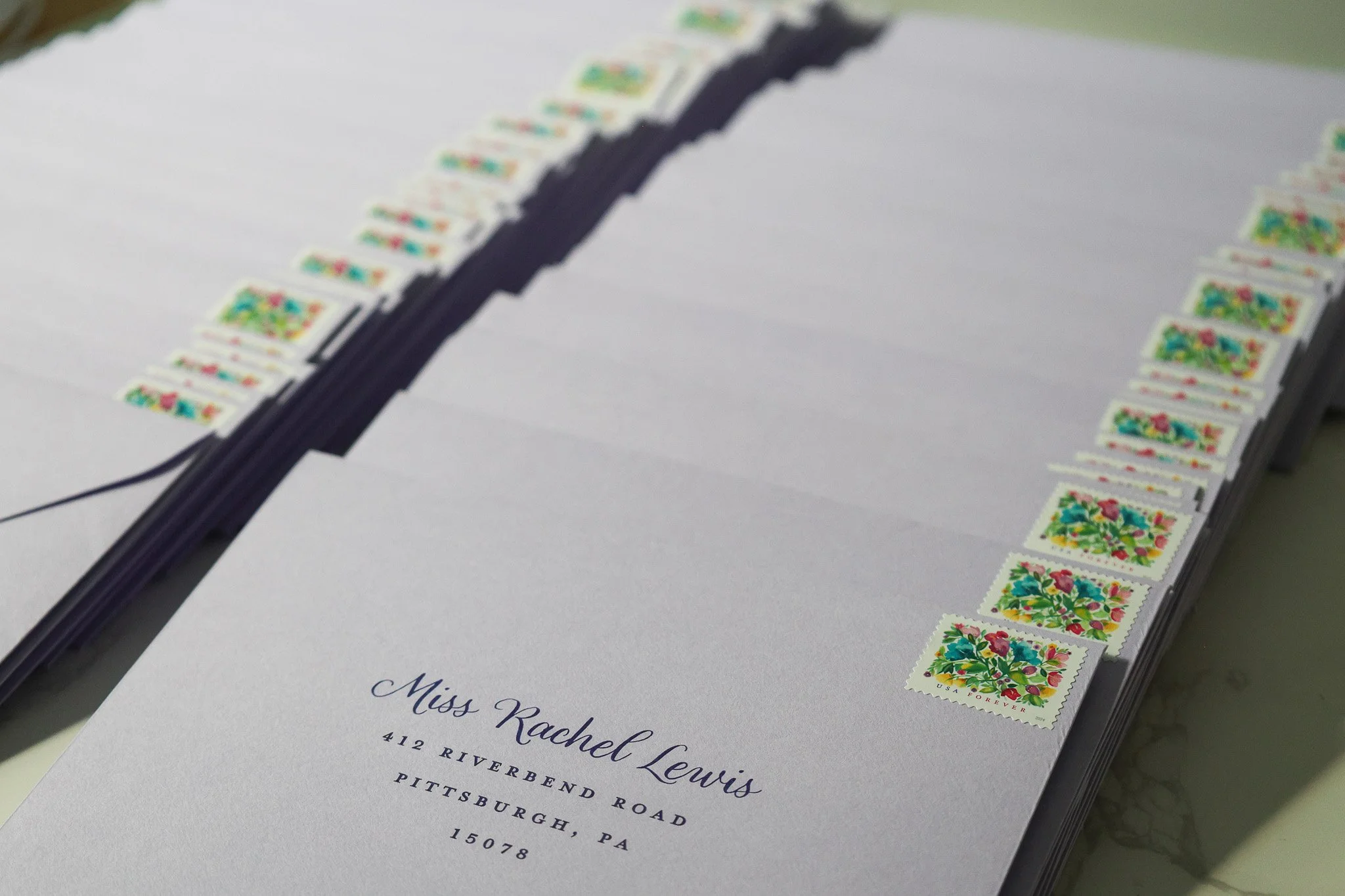 A stack of white envelopes with colorful postage stamps on the top right corner. The front envelope displays the recipient's address to Pittsburgh, PA.